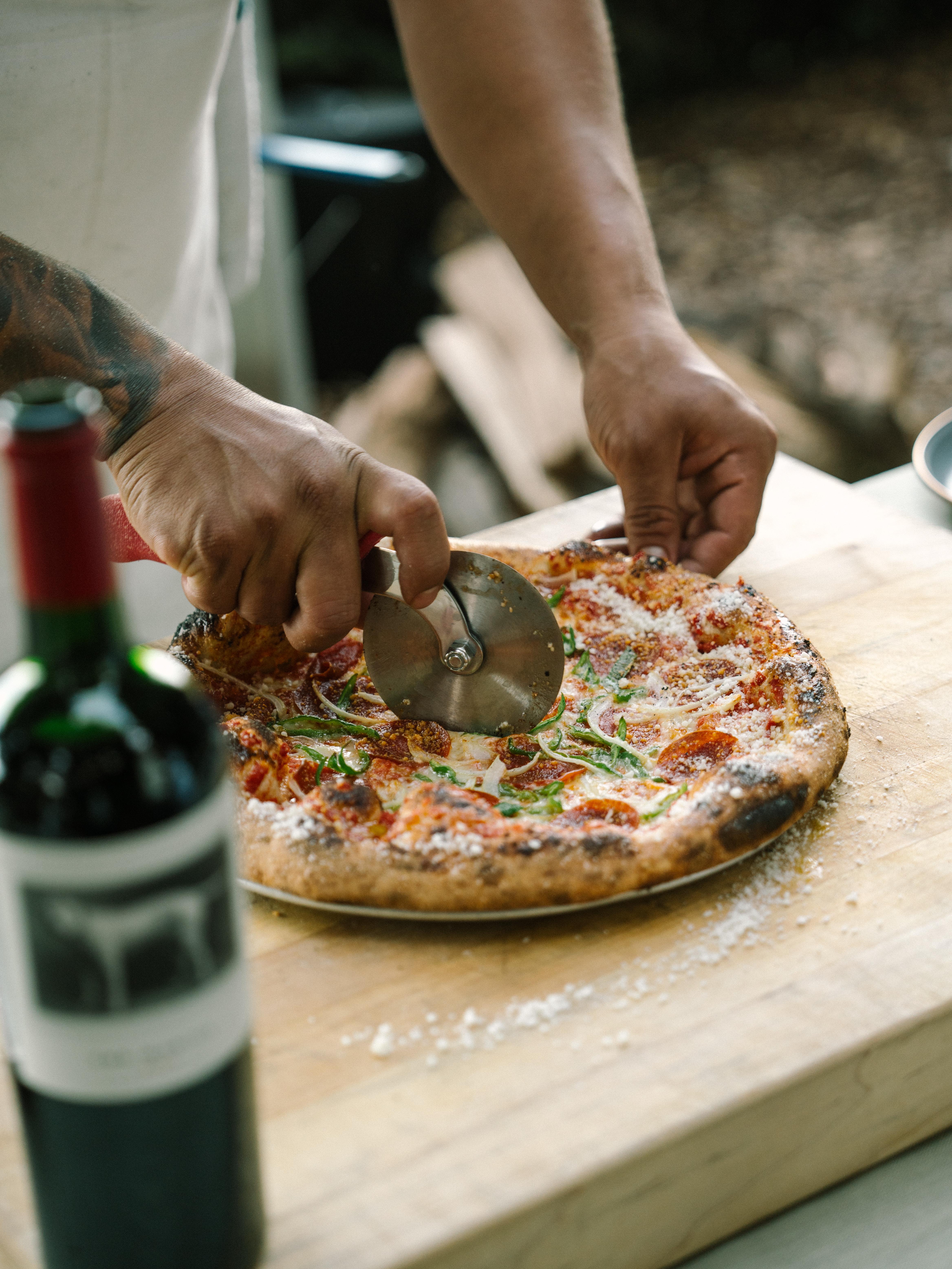 Chef slicing hot pizza next to a bottle of the mascot.