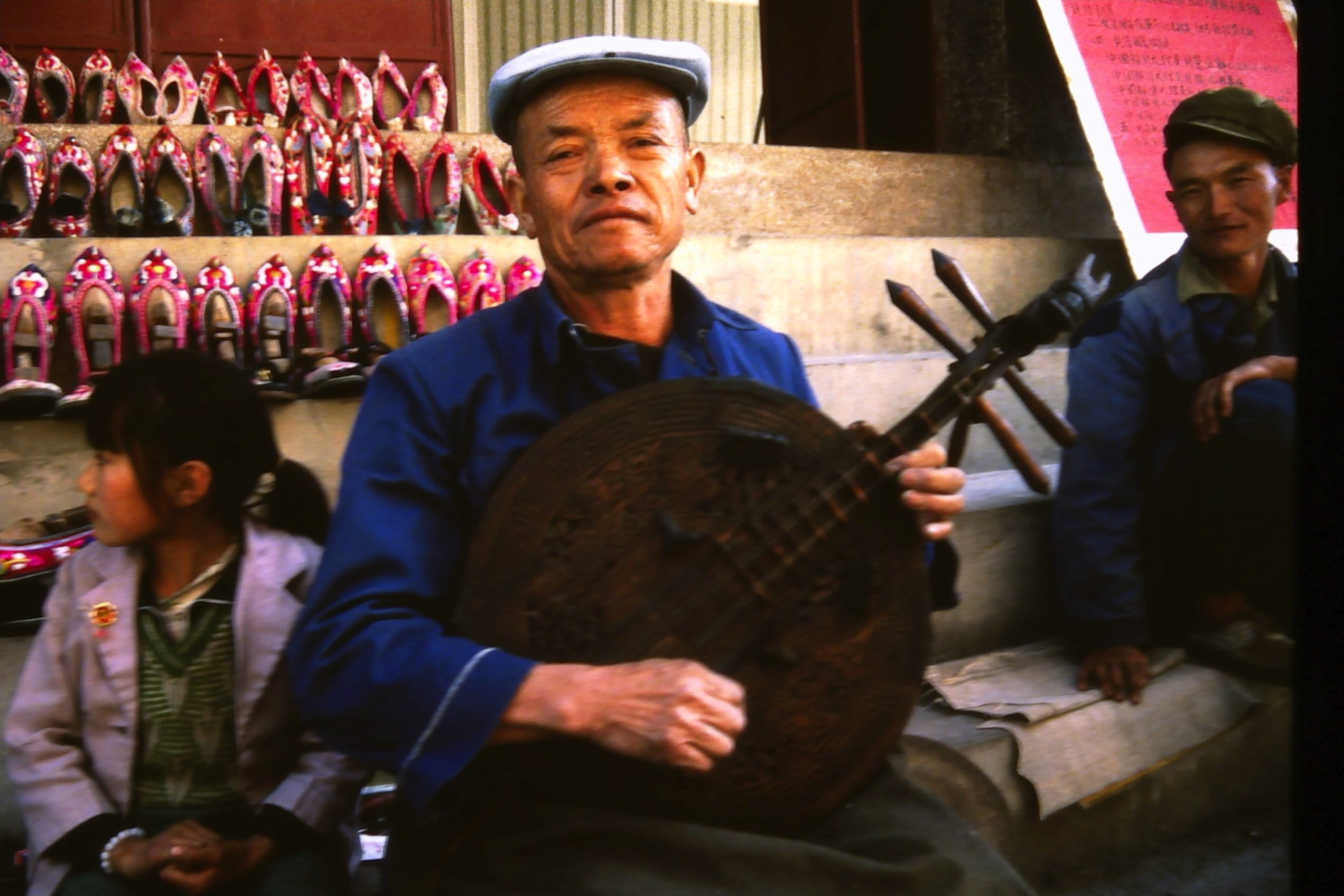 Shoe seller proudly holding his home made string instrument.