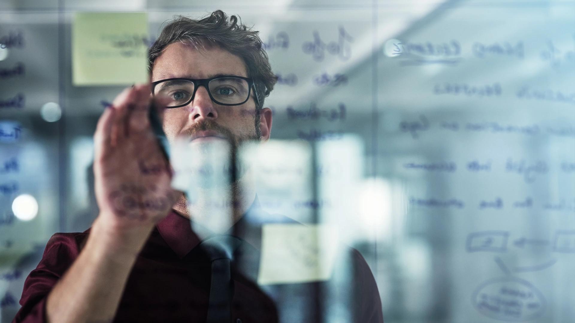 Man brainstorming and writing on a glass board with sticky notes, illustrating strategic planning and problem-solving for AI development at https://codeautomation.ai/
