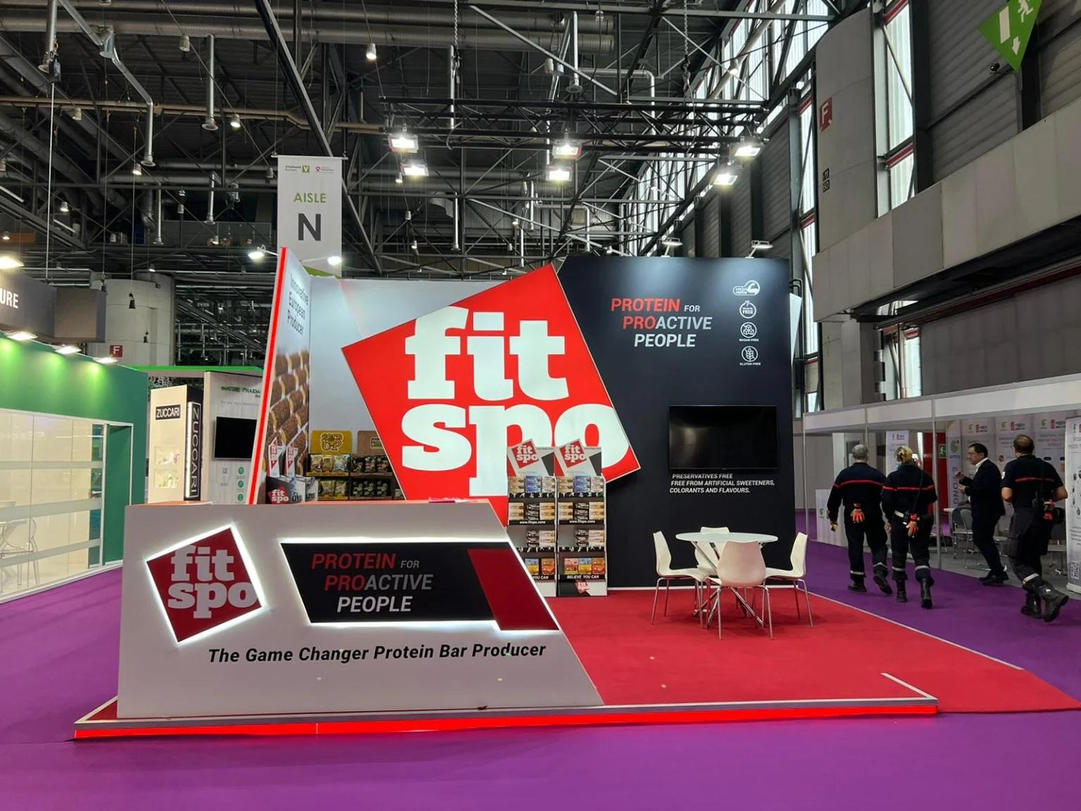 Front view of the FitSpo stand at Vitafoods Europe in Geneva, with an illuminated counter and oversized red and white logo.
