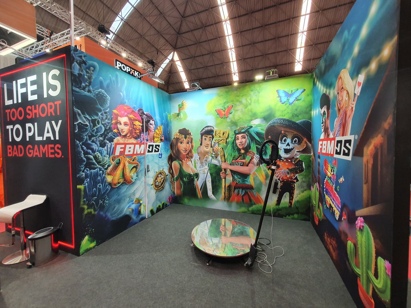 Gráfica de personajes de juegos y plataforma circular con anillo de luz en el stand de FBMDS