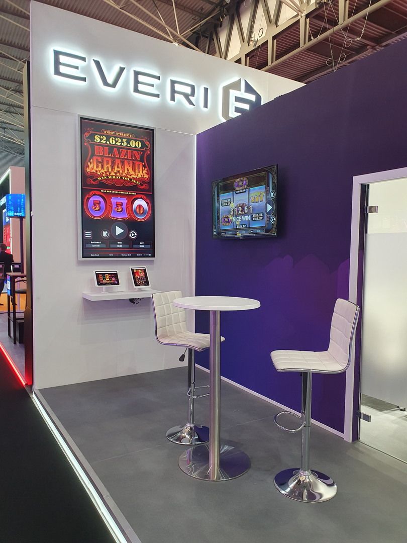 Everi demonstration area with vertical screen, tablets and a high table beside the purple wall