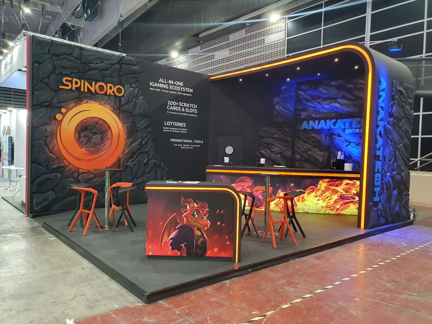 Vista general del stand de Anakatech y Spinoro en ICE Barcelona 2025, con paredes de roca artificial y marco iluminado naranja