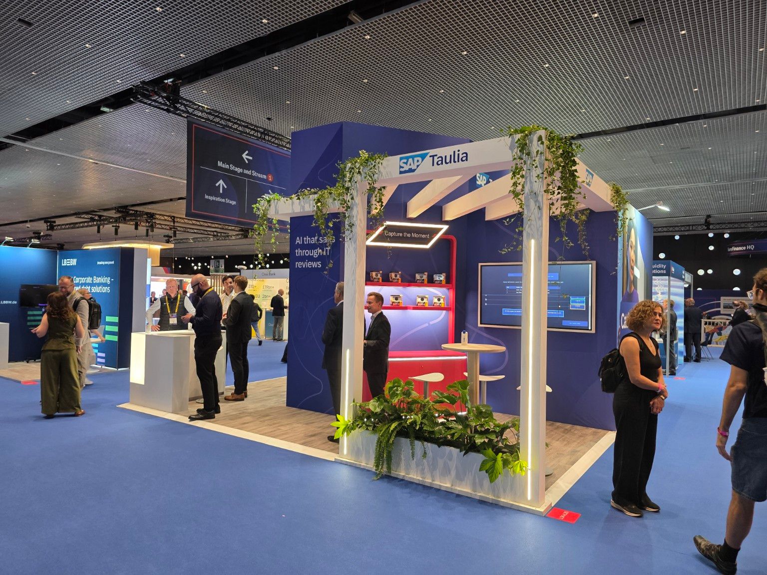 Side view of the SAP Taulia stand with a white structure, planters and demonstration screen