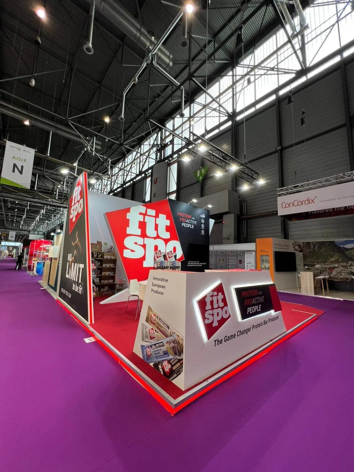 Corner view of the FitSpo stand, with an illuminated white counter and red platform at Vitafoods Geneva.