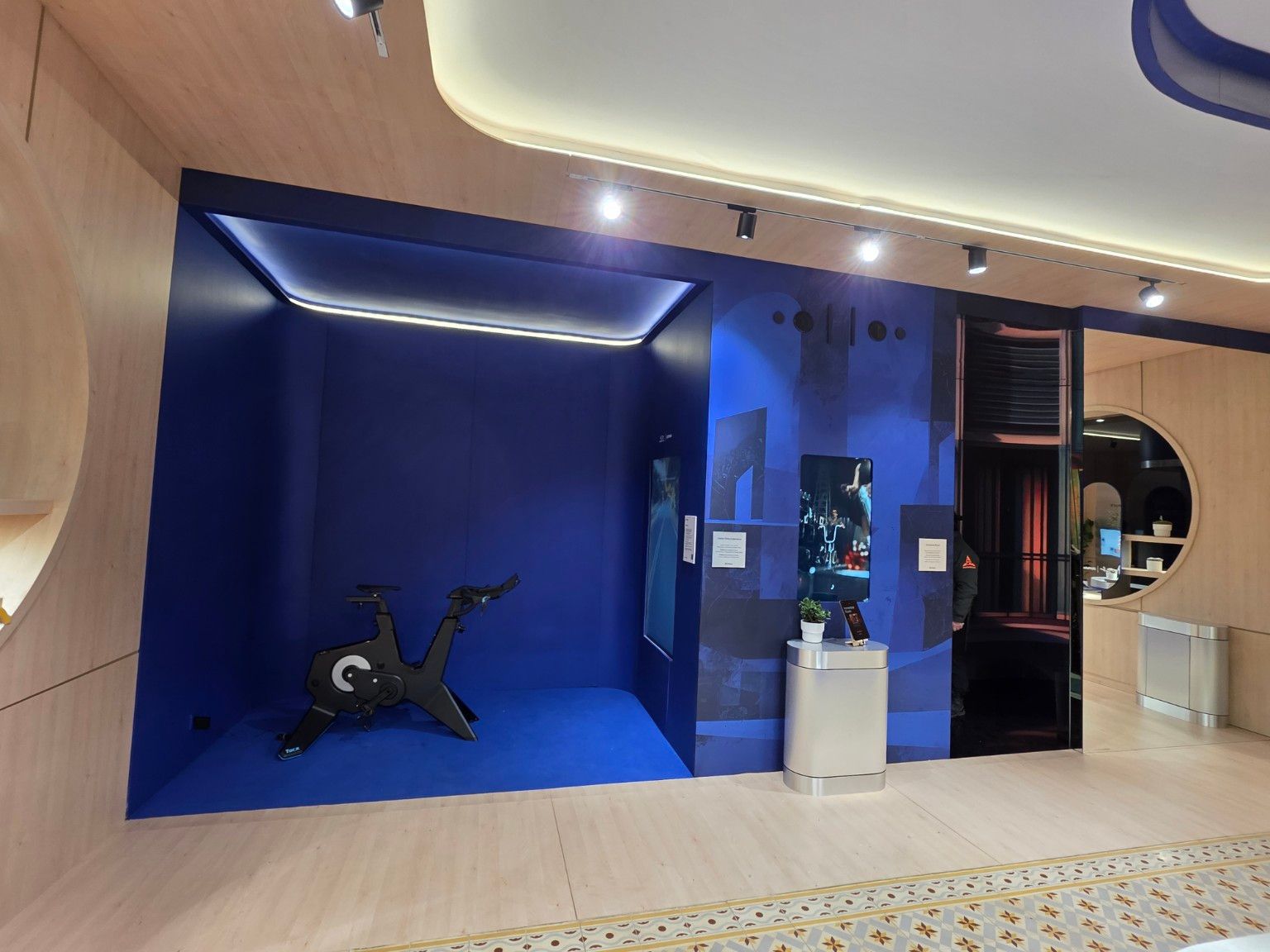 Blue demonstration area with a stationary bicycle, vertical screen and perimeter lighting