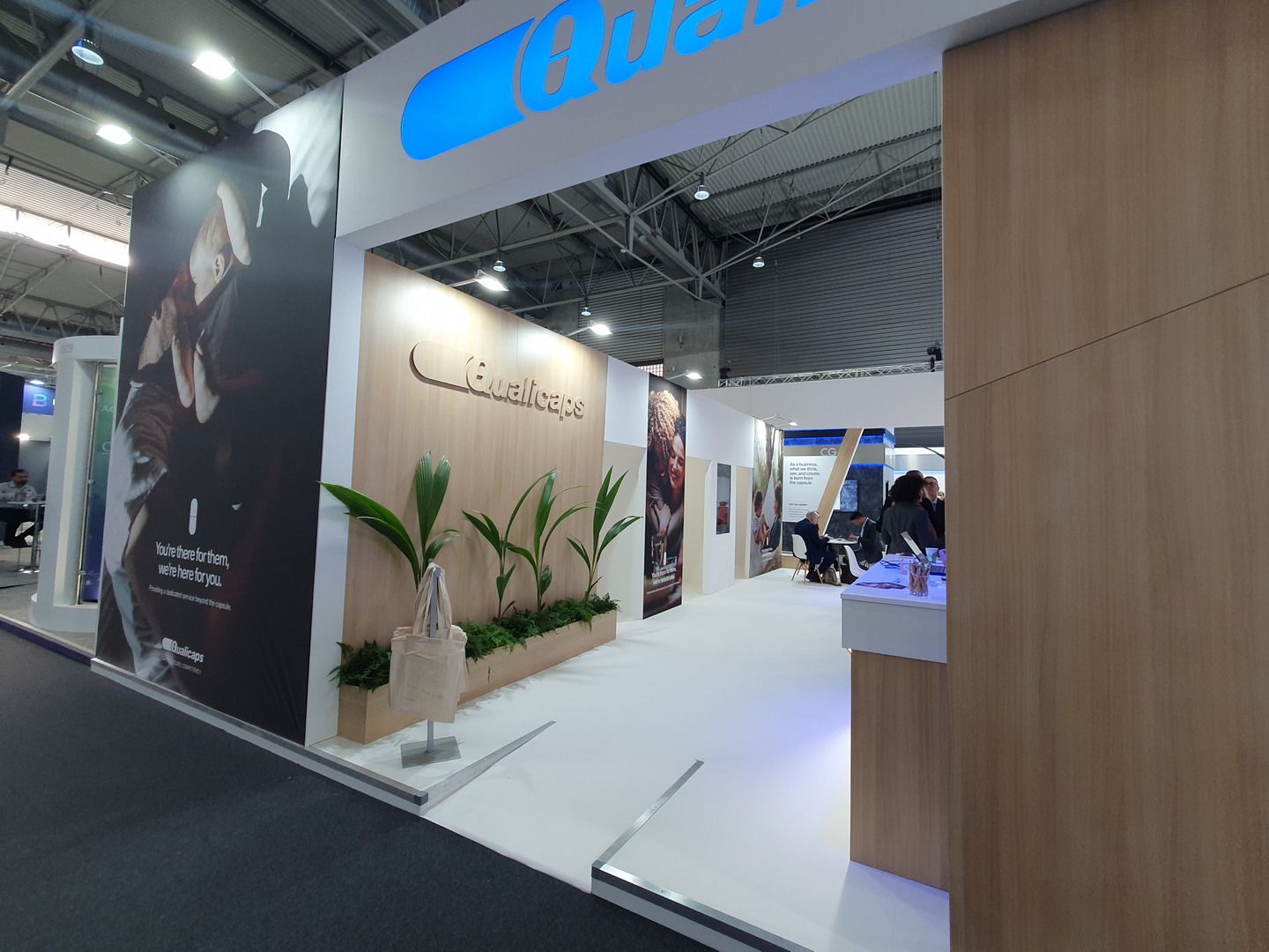 White portal, timber and blue Qualicaps sign — Qualicaps · CPHI