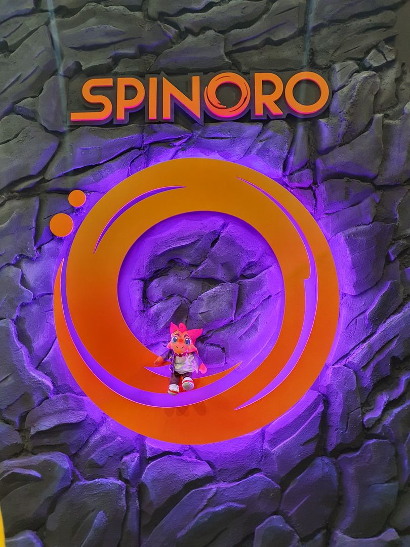 Orange Spinoro logo on an artificial rock wall with violet lighting and mascot