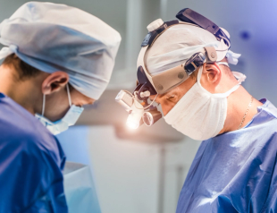 Two surgeons looking down, one wearing headlight