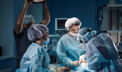 Nurse holding light above 3 surgeons while they operate