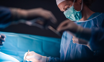 Surgeon handing tool to another surgeon in foreground, another surgeon in background