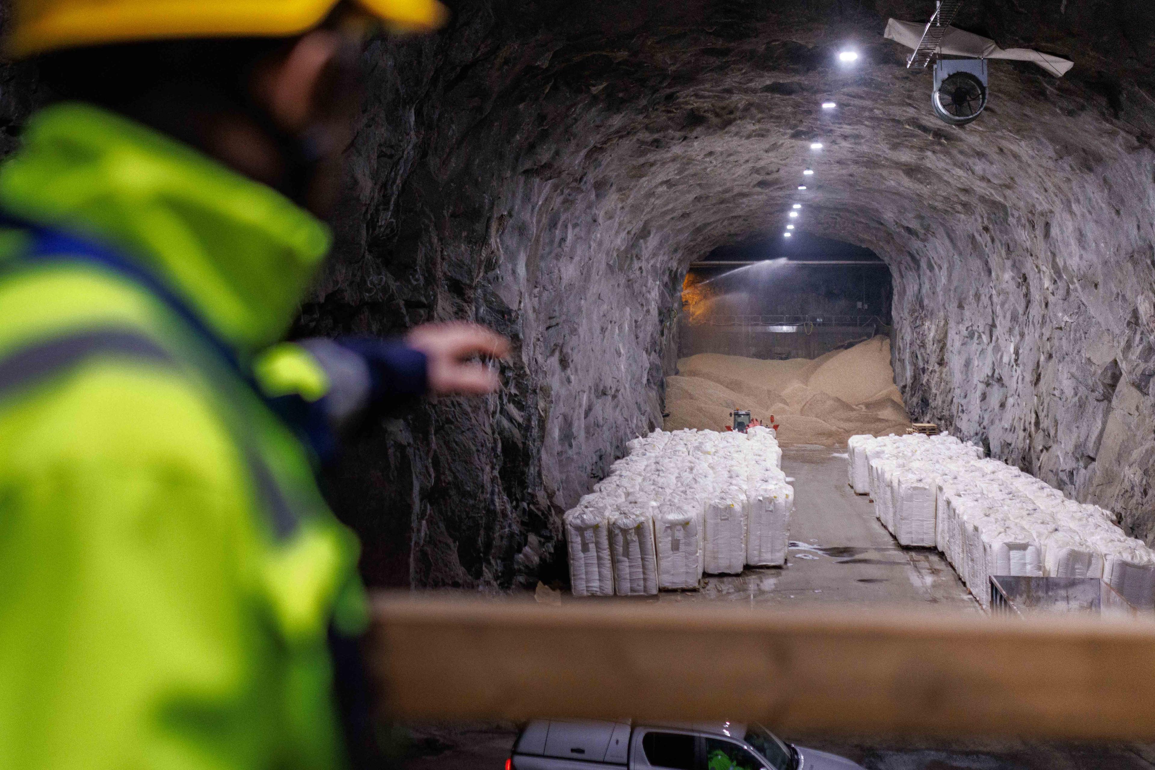 En mann i signalgule arbeidsklær peker mot en tunnel med pellets og hvite sekker.