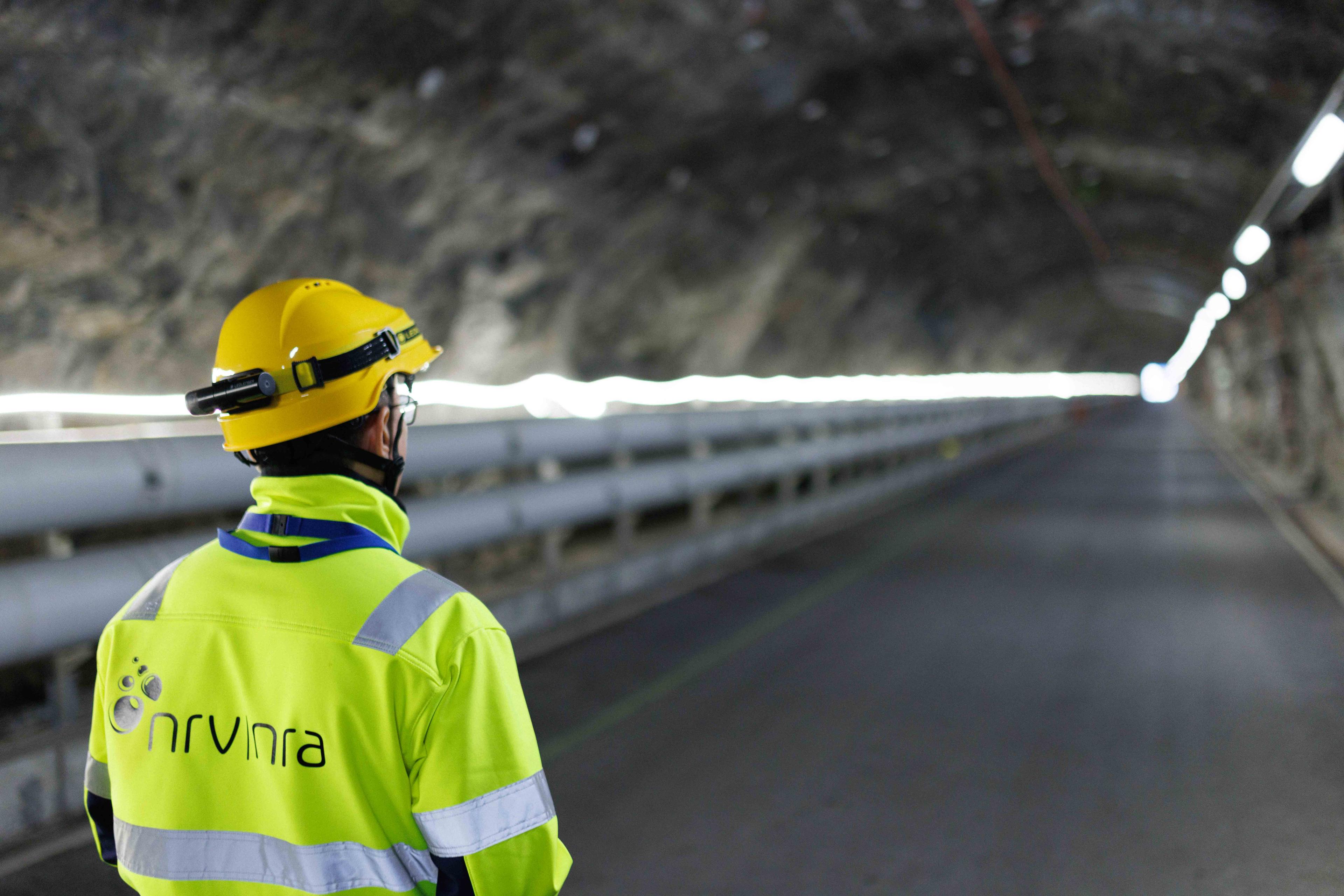 En mann i gule verneklær står med ryggen til og ser innover i en tunnel.