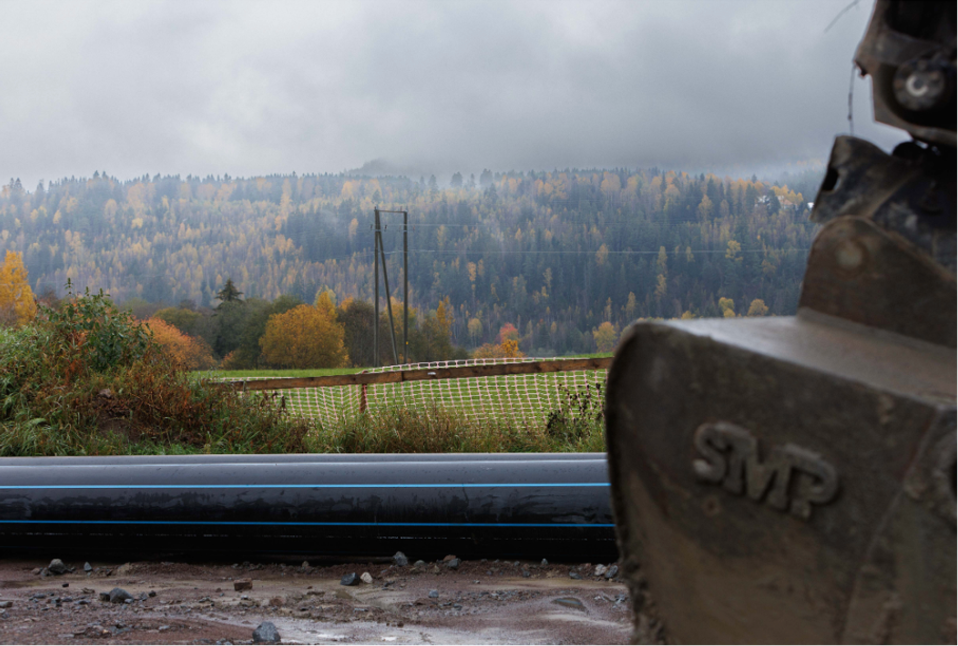 Vannledning i et anleggsområde med høstfargede fjellskoger i bakgrunnen under en overskyet himmel.