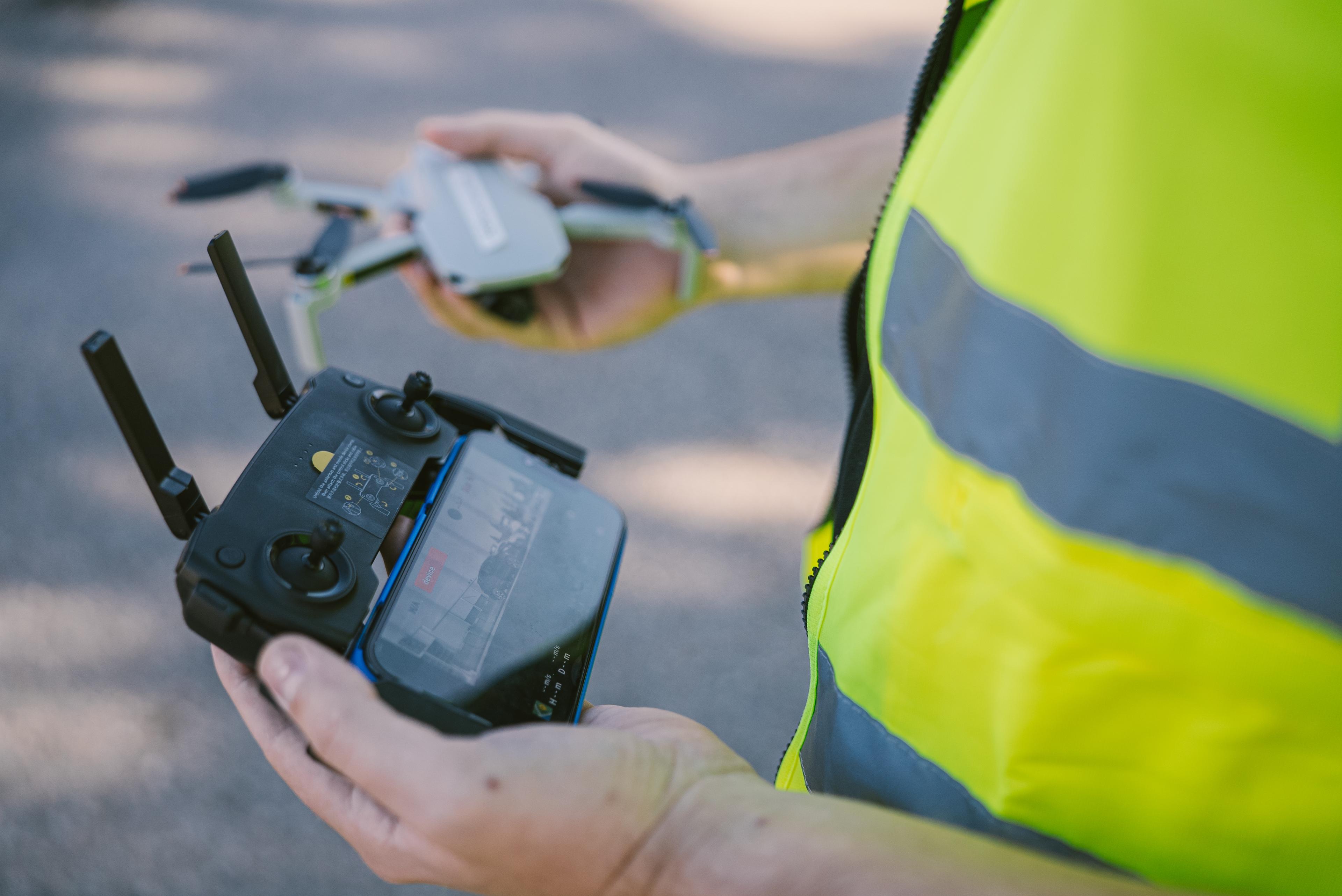 Nærbilde av droneoperatør med fjernkontroll, iført refleksvest