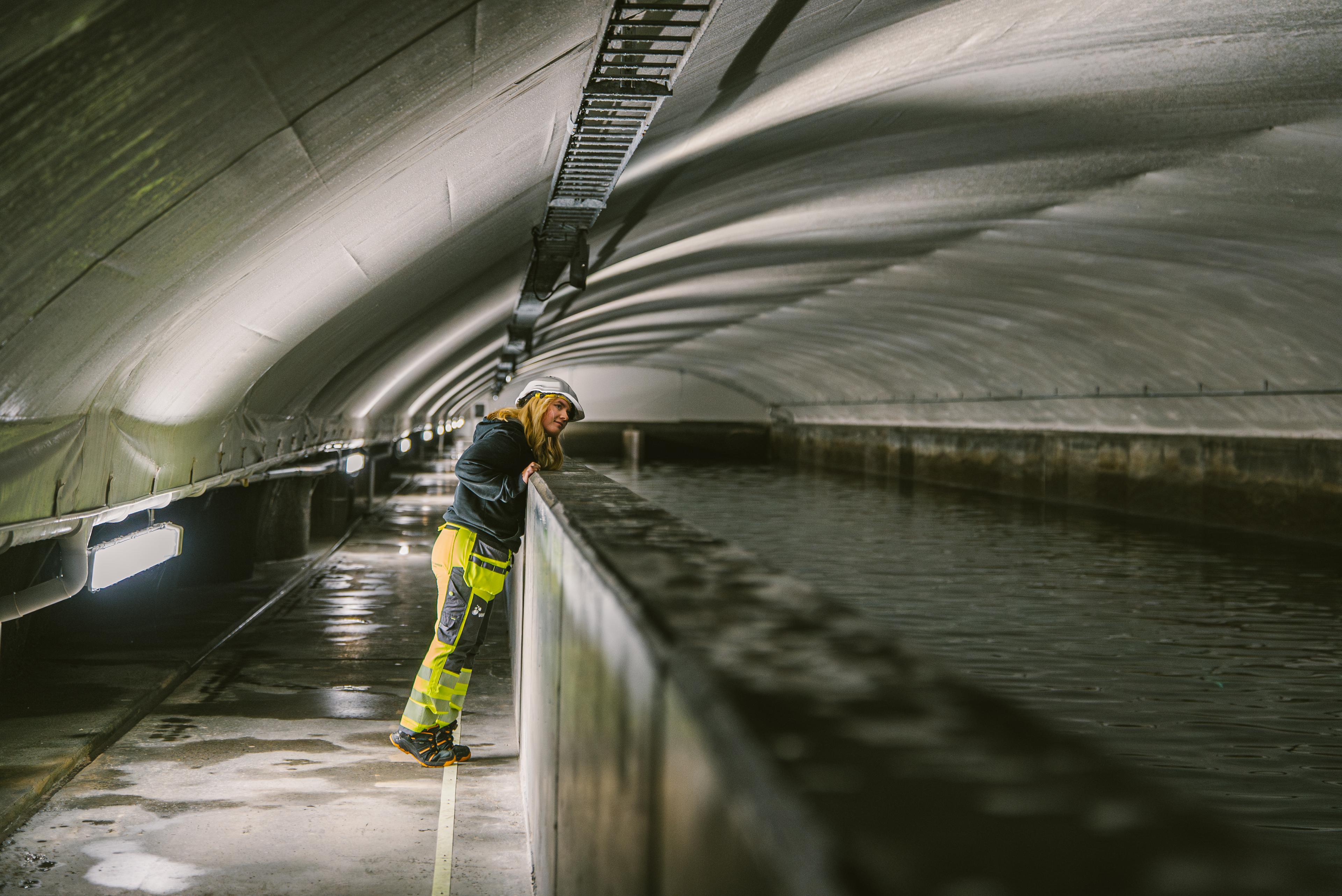 Ansatt i refleksvest og hjelm inspiserer en tunnel eller rørledning med buede vegger