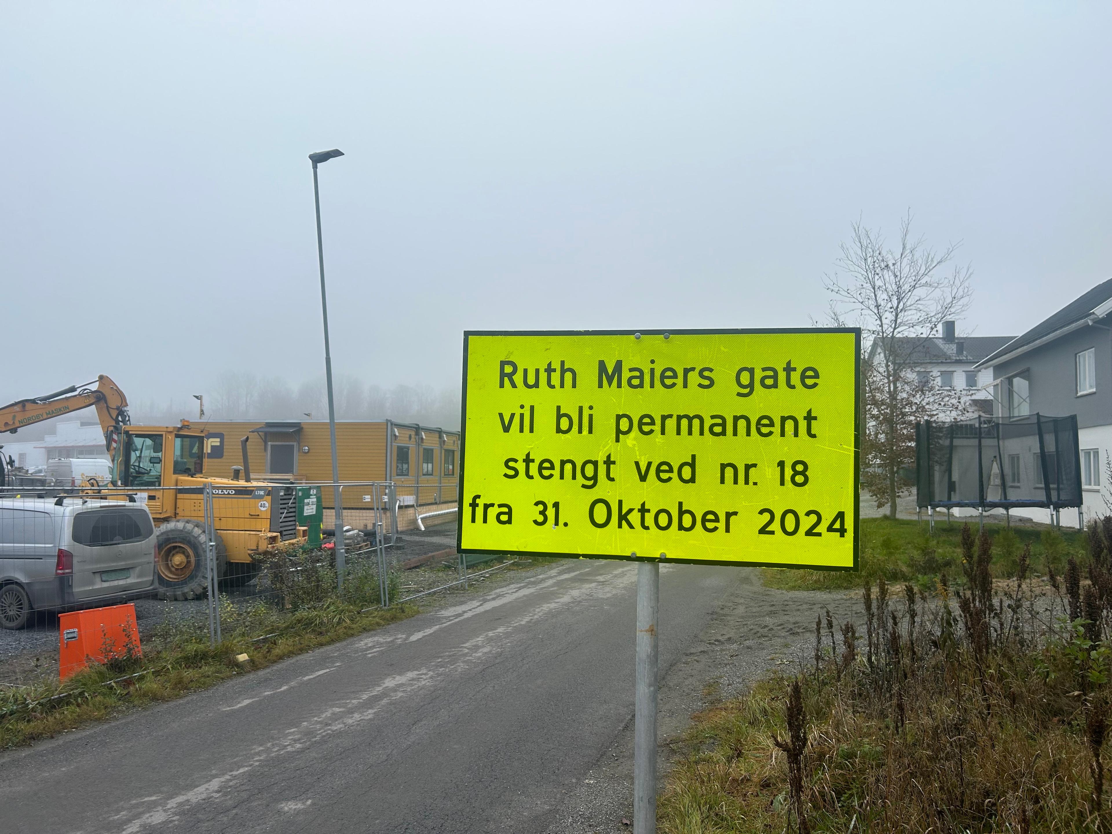 lt anleggsskilt som varsler at "Ruth Maiers gate vil bli permanent stengt ved nr 18 fra 31. Oktober 2024" ved byggeplass med anleggsmaskiner og brakker i bakgrunnen.