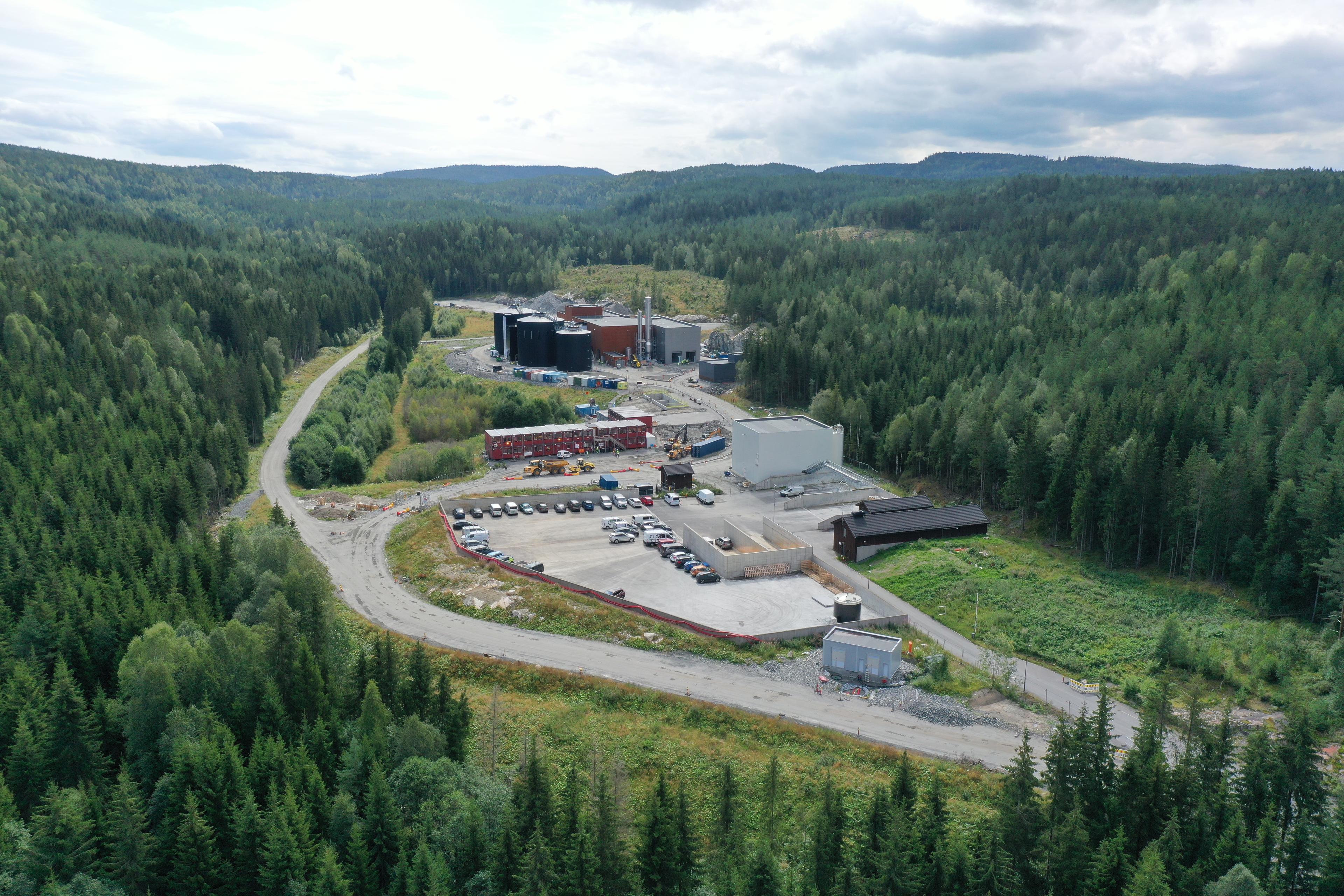 Flyfoto av Biogass Krogstad-anlegg, omkranset av tett granskog med parkeringsplass og industribygg