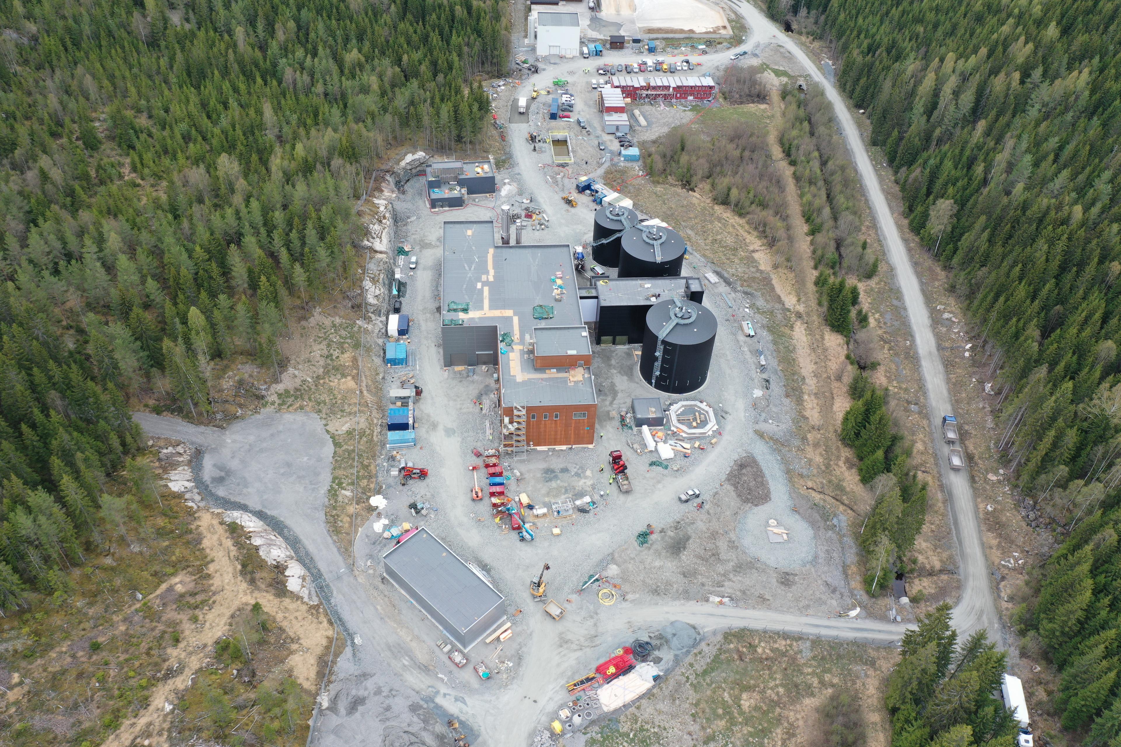 Flere lystbåter fortøyd ved brygge, med bro og grønne skosskråninger i bakgrunnen