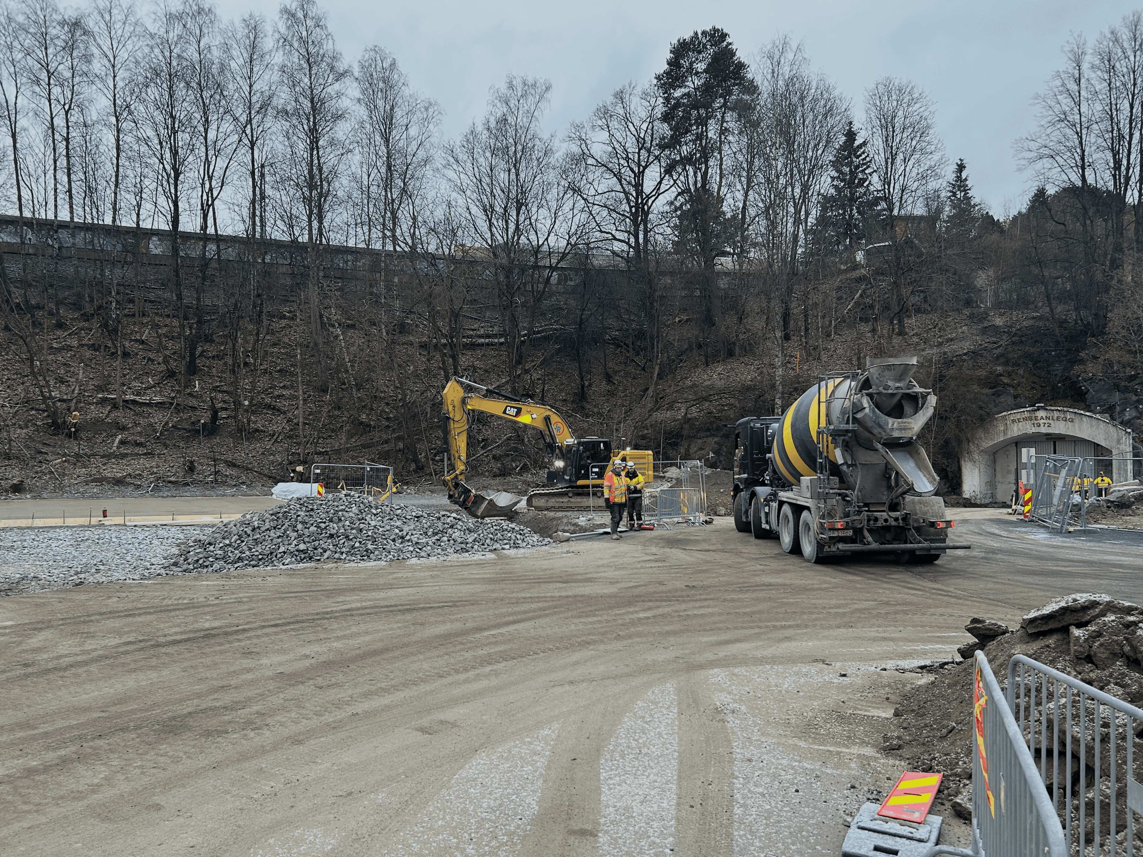 Betongbil og gravemaskin foran tunnelåpning på anleggsplass. 