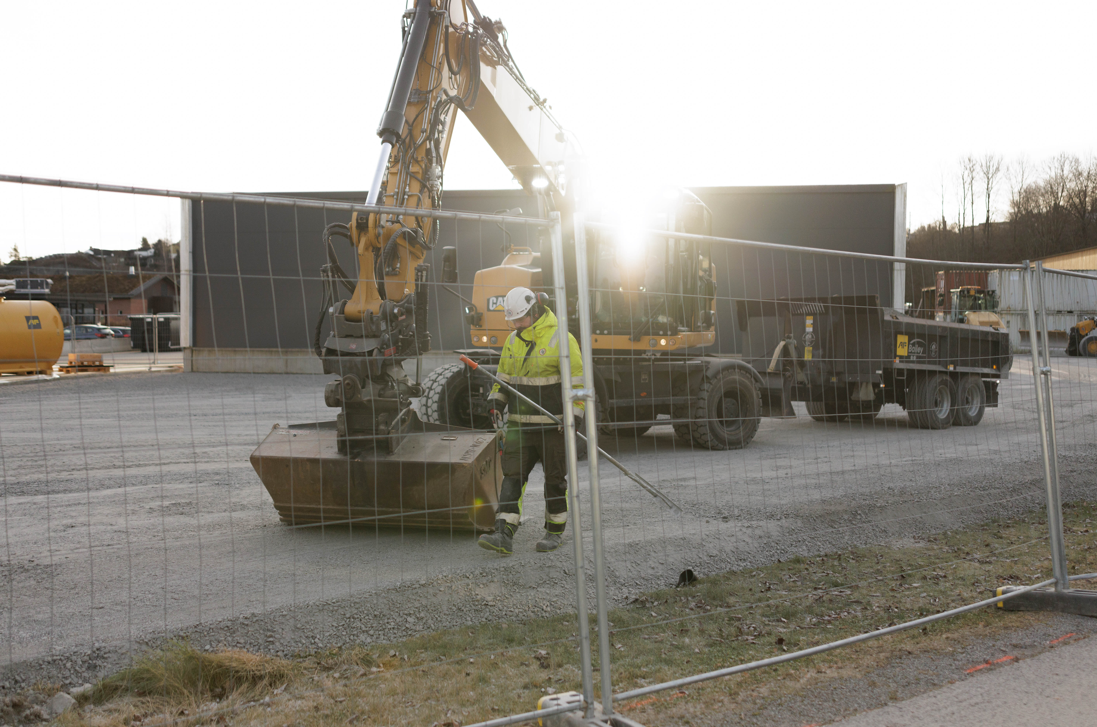 En mann i gul refleksjakke går forbi en gravemaskin