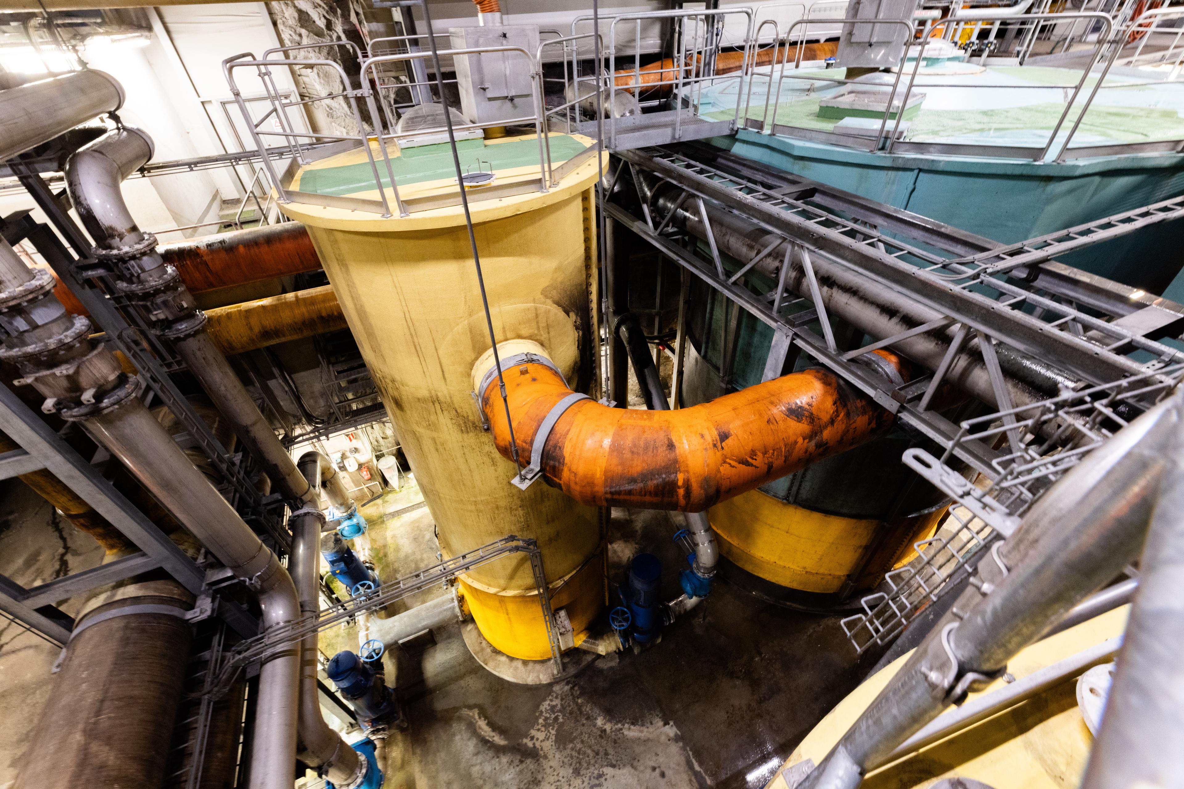 Interiør fra RA2 renseanlegg, som viser en gul tank med tilkoblede oransje og grå rør, og metallgangveier over