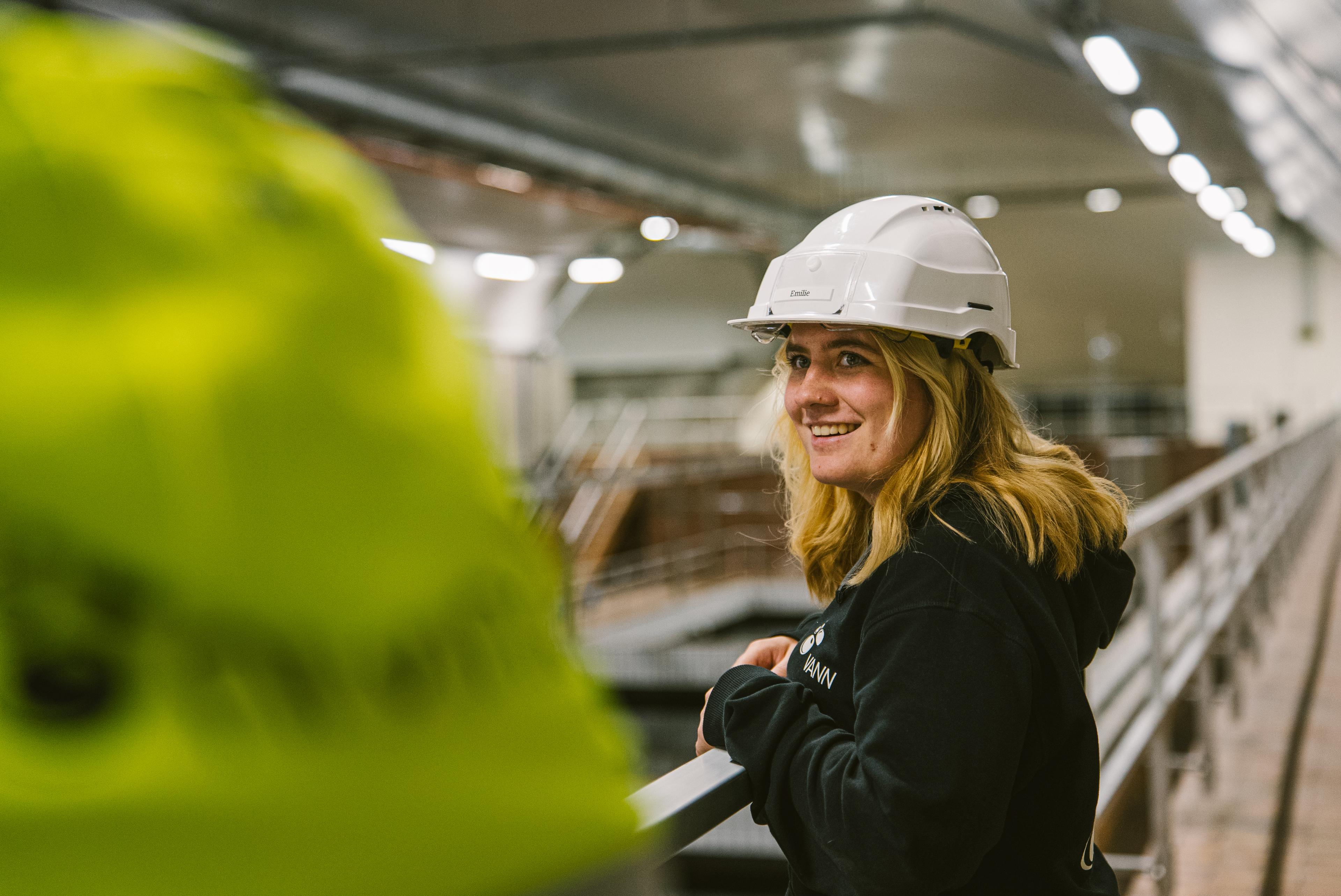 arbeider i hvit hjelm og svart firmagenser som smiler til kamera.