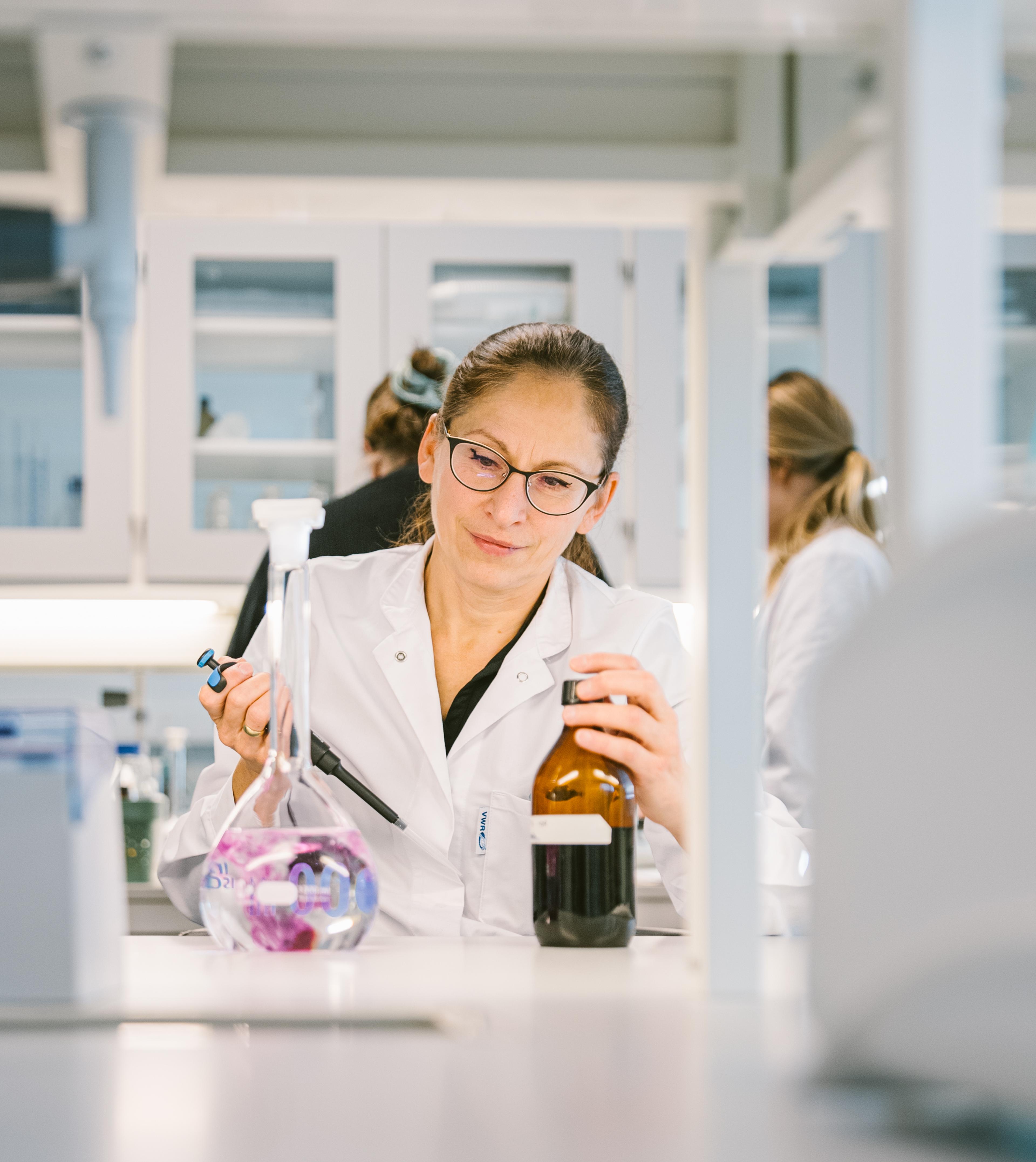 Kvinnelig forsker i hvit laboratoriefrakk arbeider med prøverør i et moderne laboratorium