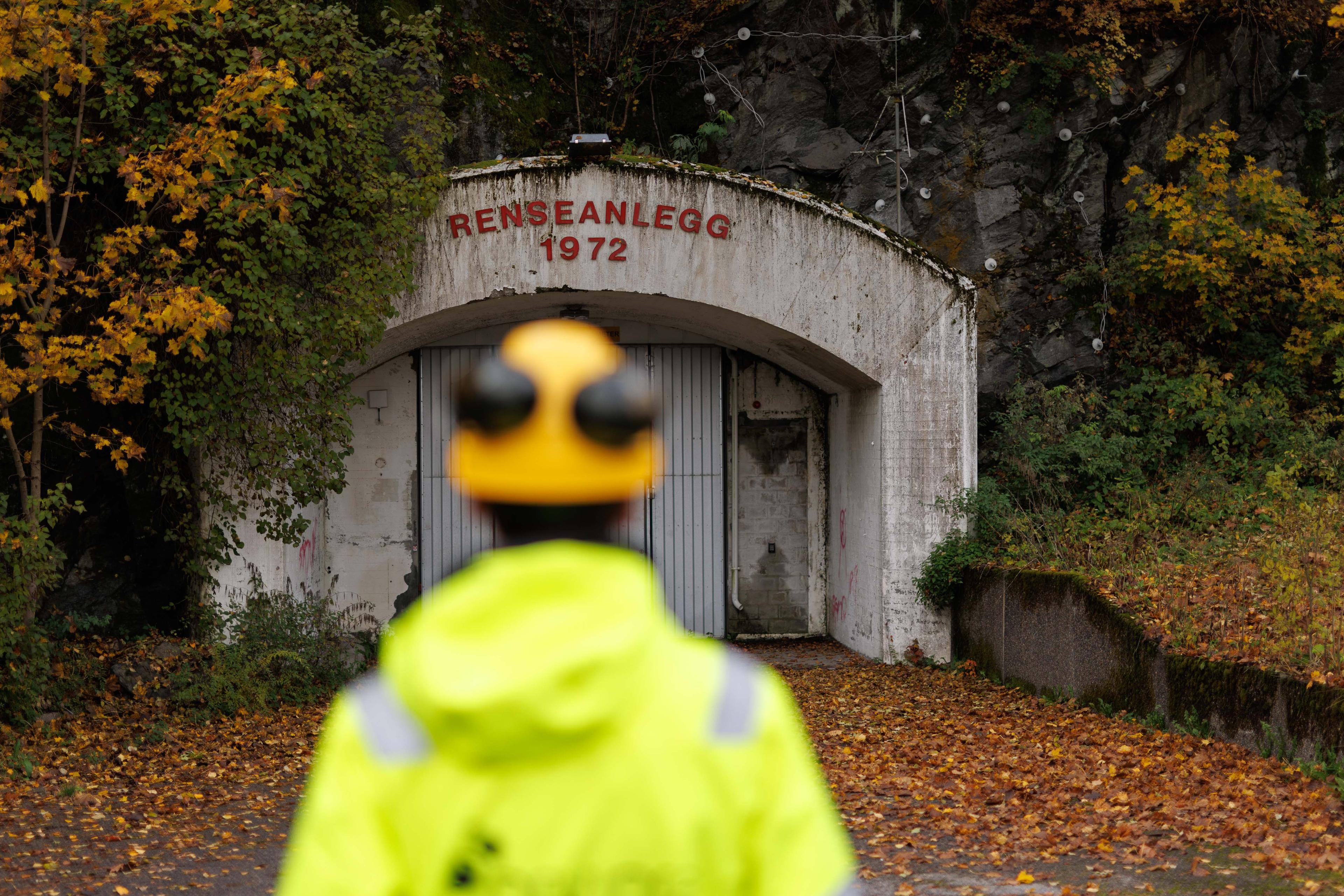 Arbeider i refleksvest foran gammel tunnelinngang merket "Renseanlegg 1972", omgitt av høstlige trær