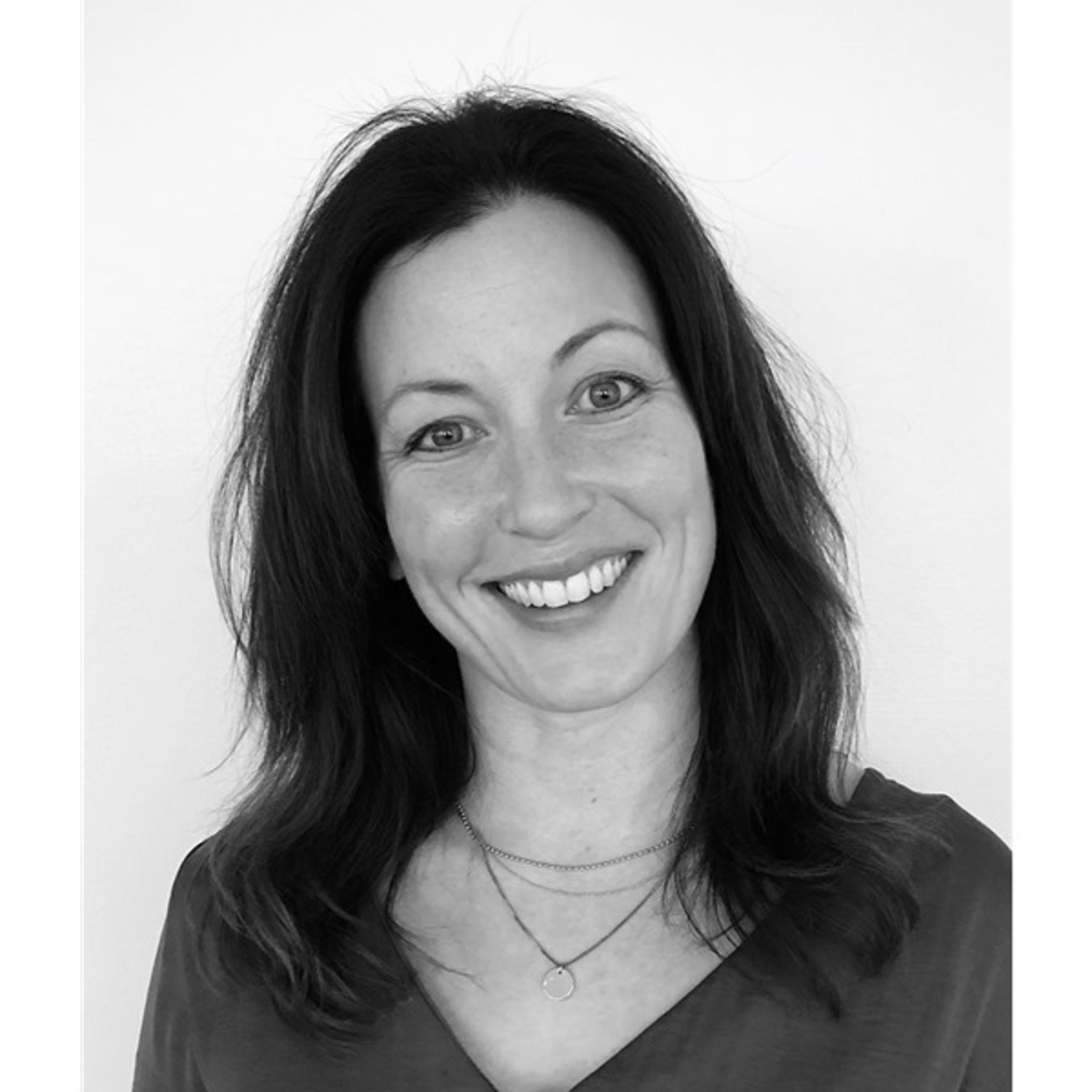 Kvinne med mørkt hår og stort smil i svart-hvitt portrettfoto.