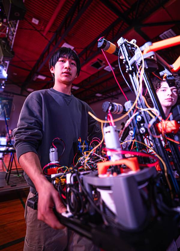 Une personne travaille sur un robot rempli de câbles sous un éclairage rouge et violet dans un atelier ou un espace de compétition intérieur.