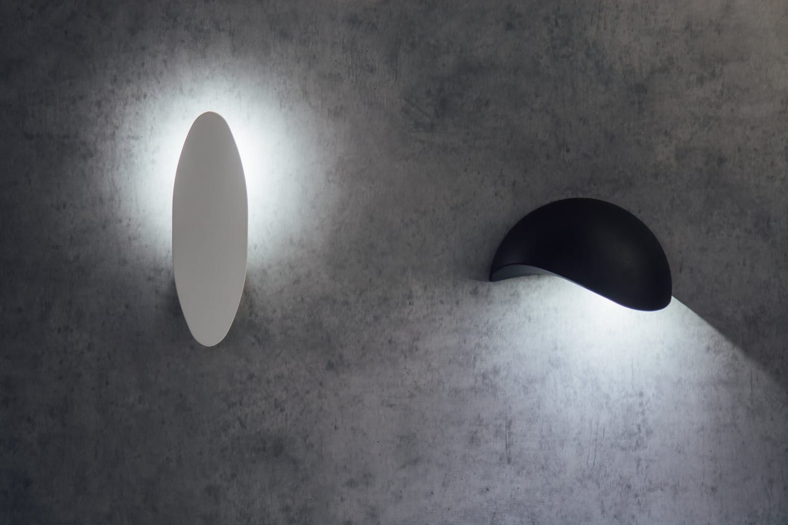 Zidne lampe na betonskom zidu — bela ovalna i crna polukružna