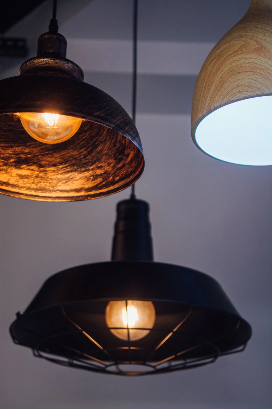 Viseće lampe industrijskog dizajna — metalna i drvena — upaljene u izložbenom prostoru SP Group.