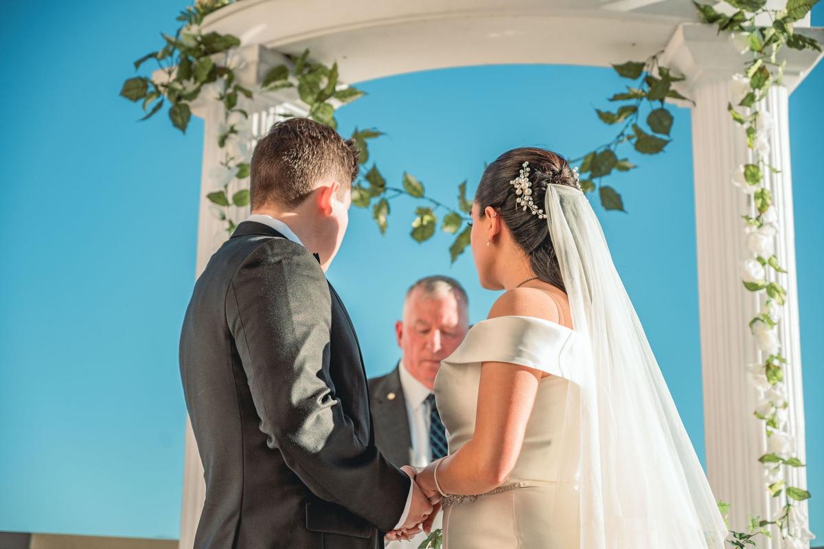 Novios tomados de la mano bajo un arco decorado con flores y follaje