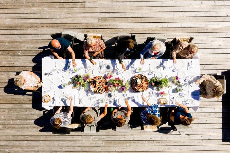 A group of happy people raise their glasses around a long table in the sun