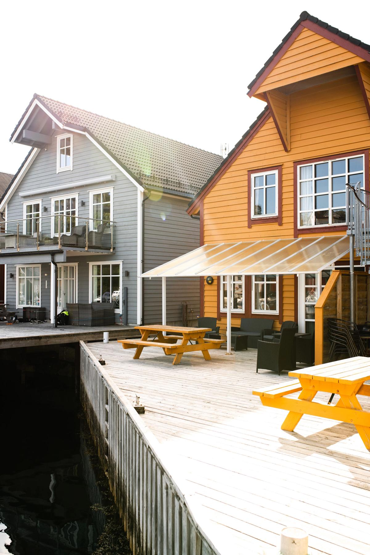 Picture of one grey and one orange cabin with outdoor tables in front on a dock.