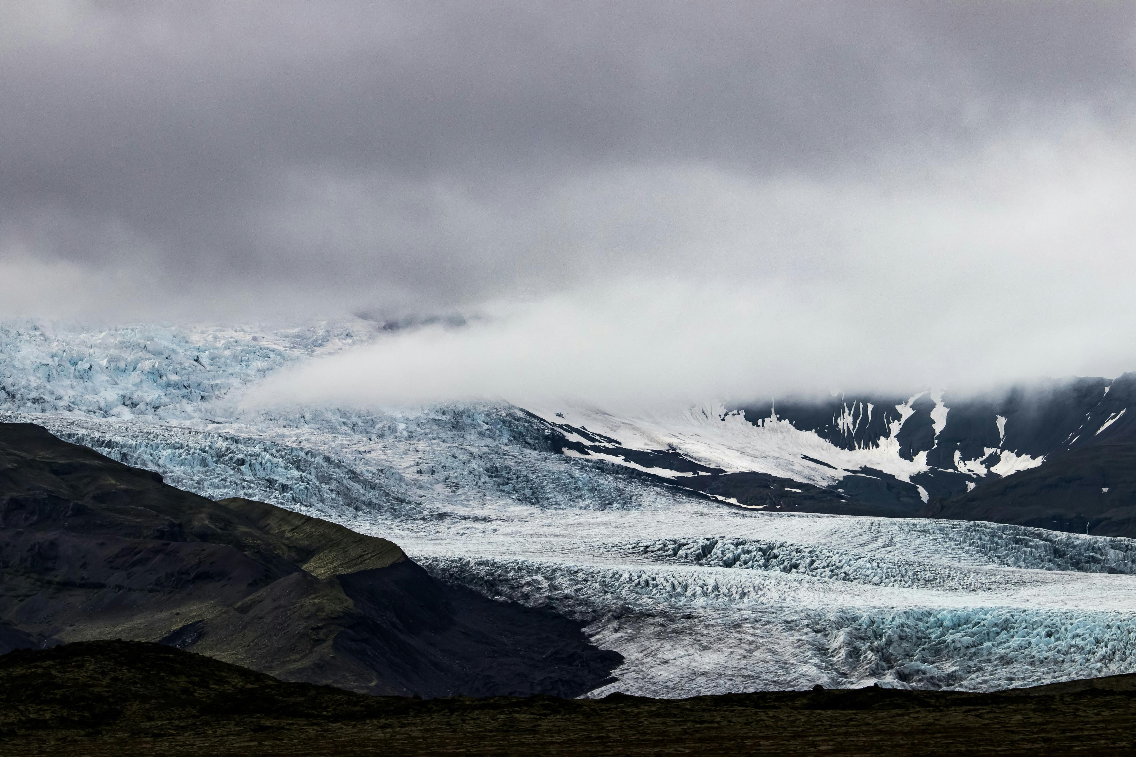 A dramatic view of Sólheimajökull glacier under heavy clouds, with blue ice stretching across the rugged landscape. A moody and breathtaking scene from a Sólheimajökull glacier hike in Iceland.