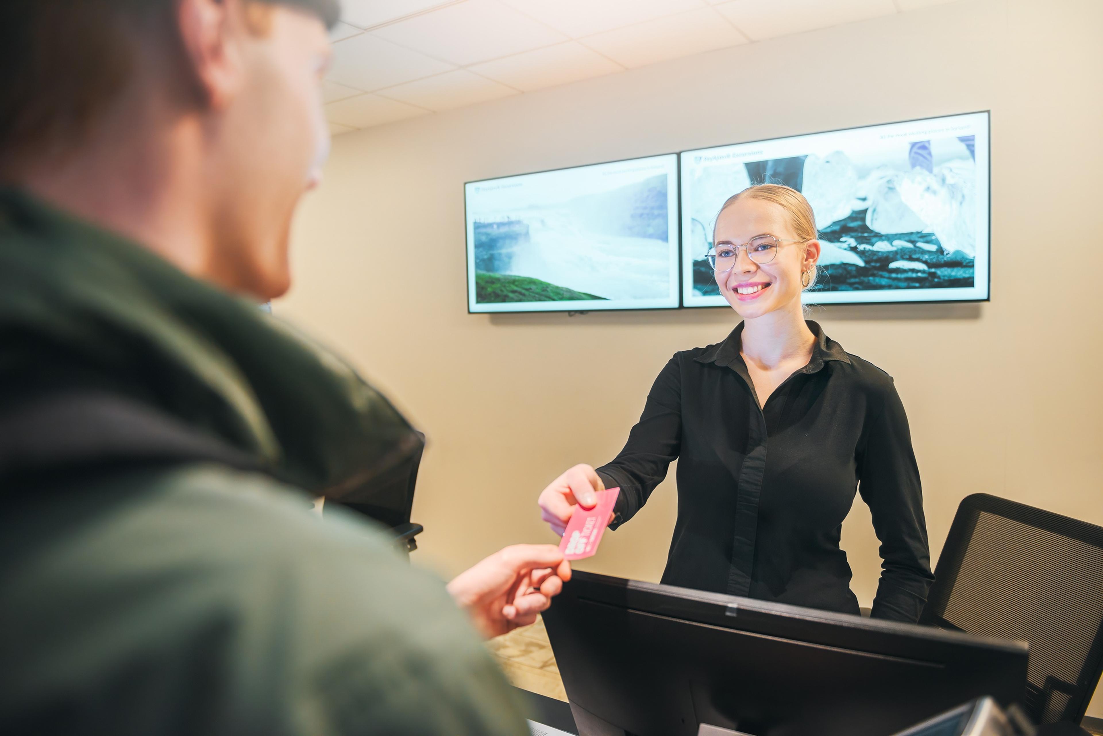 A smiling woman hands a pink card to a man at a counter.