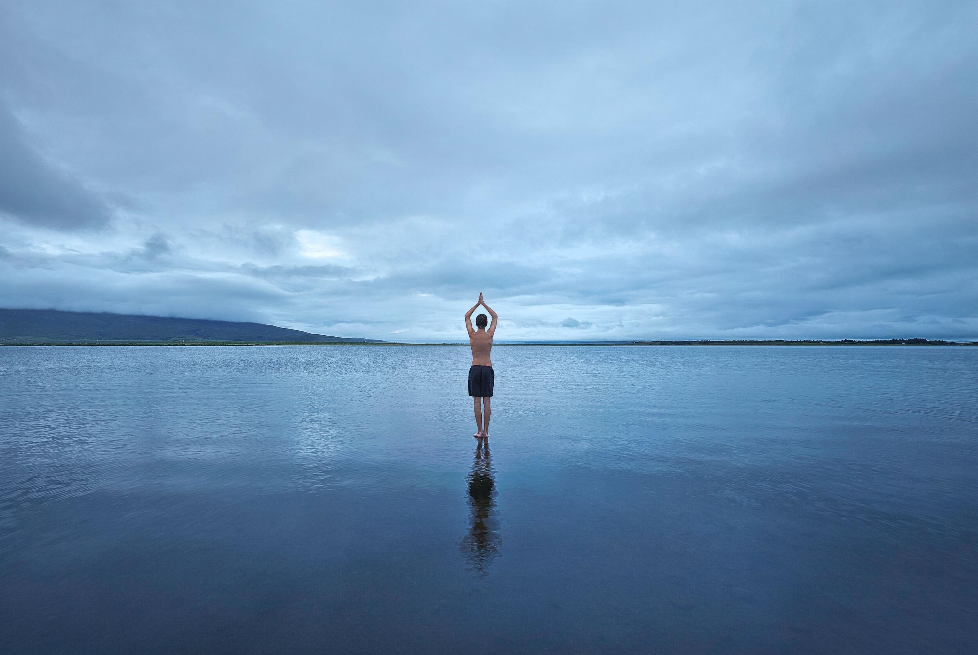 Person in a meditative pose, standing in a serene lake with raised arms, reflecting a peaceful and calm atmosphere.