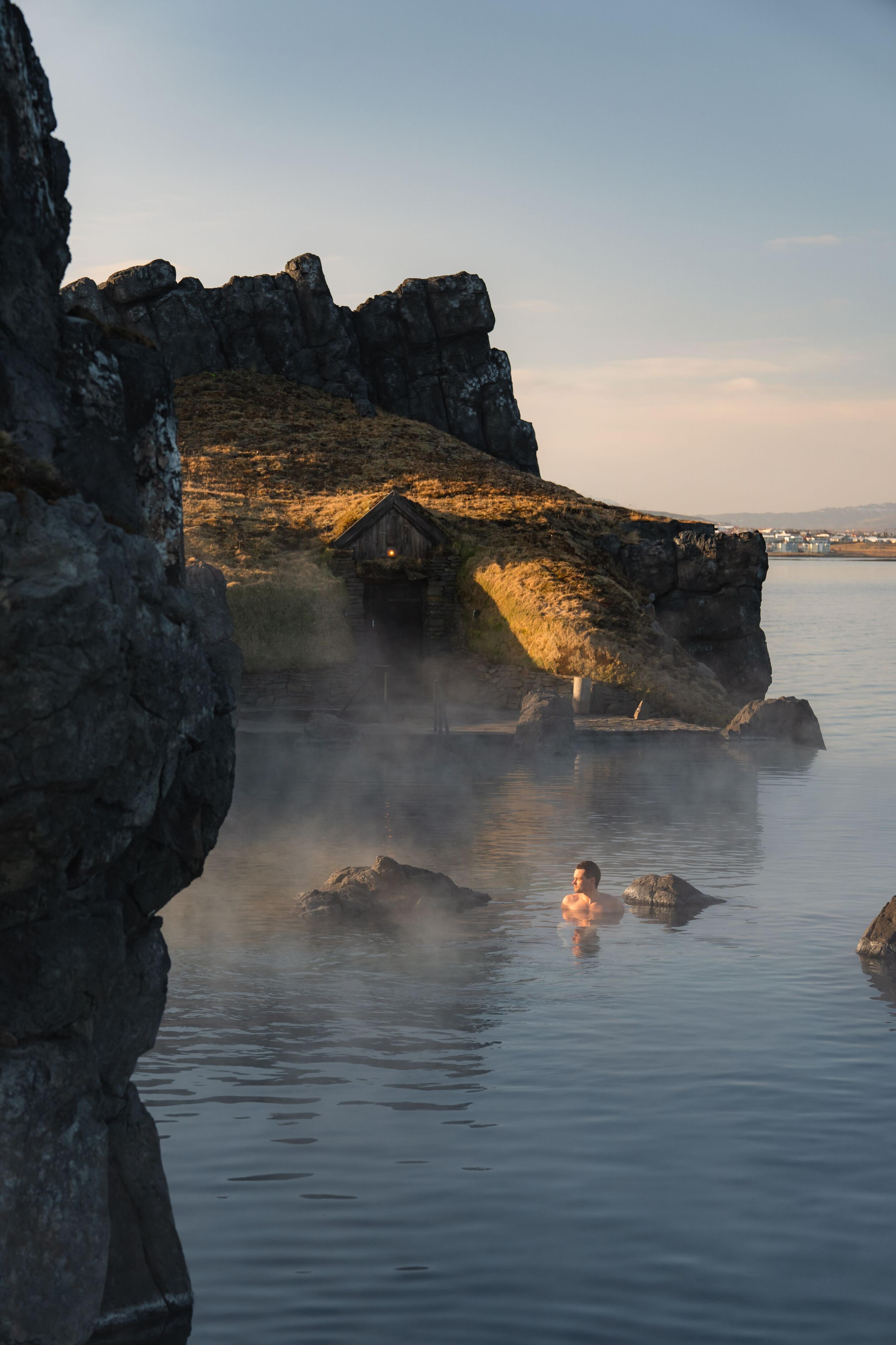 a man is swimming in a hot spring near a rocky shore .