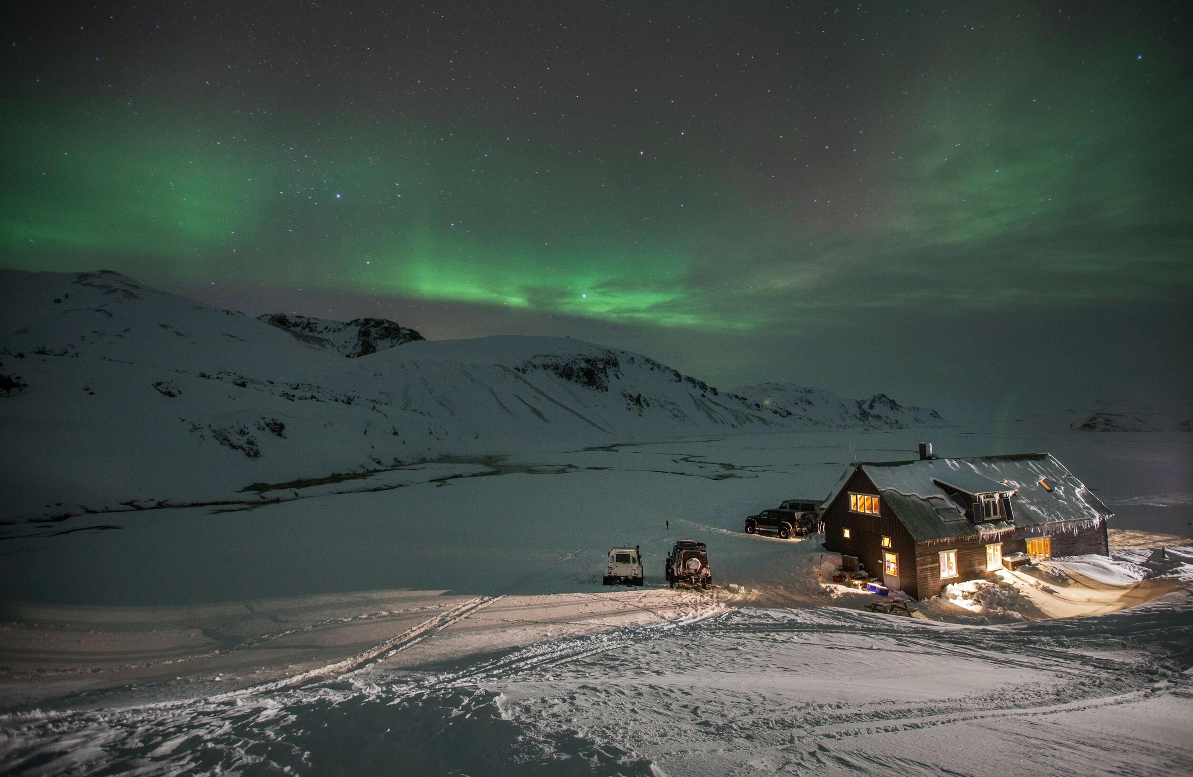 Camp setup with superjeeps under the Northern Lights in the snowy Iceland Highlands.