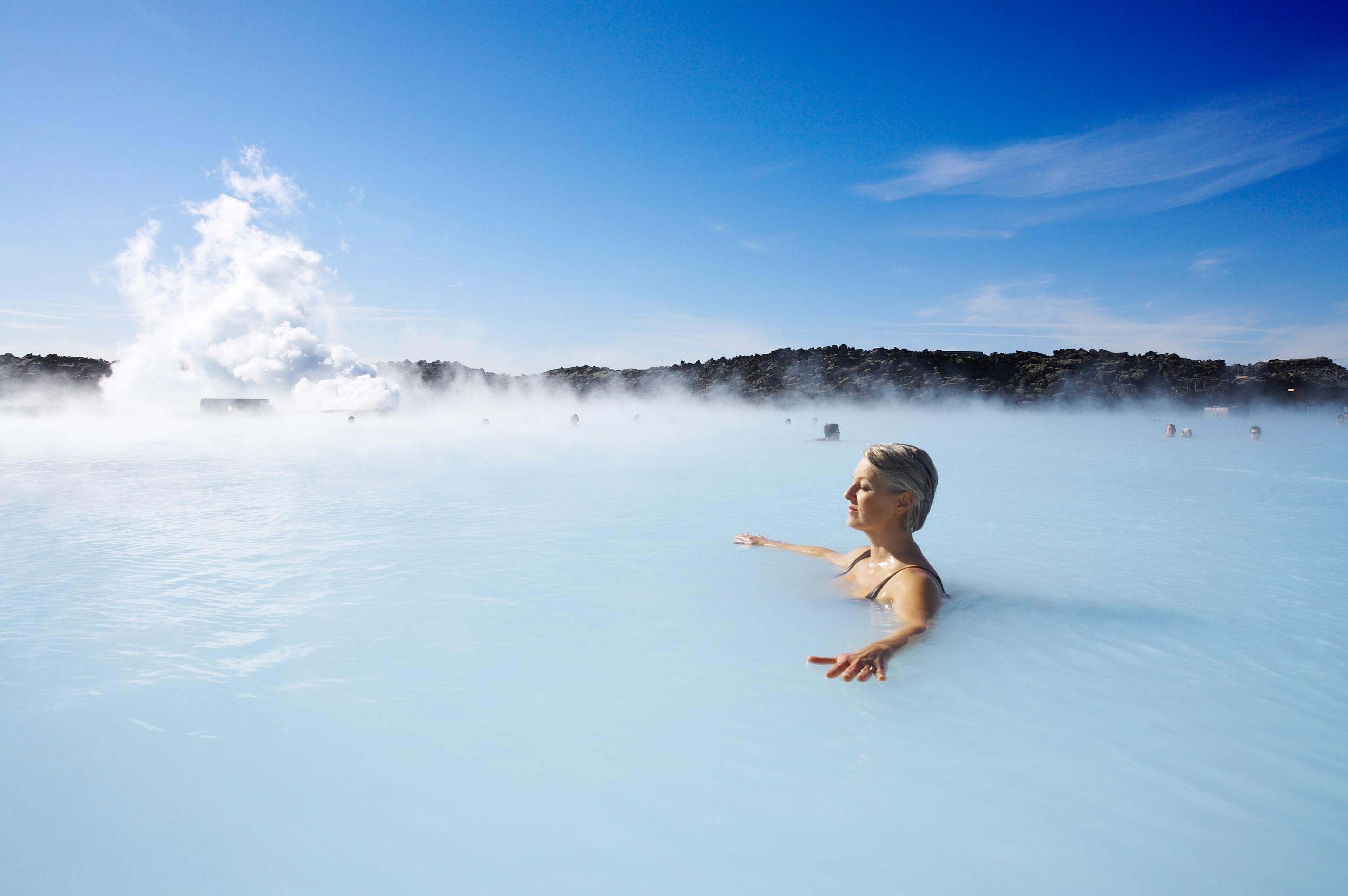 Woman relaxing in Blue Lagoon, steam and lava in background