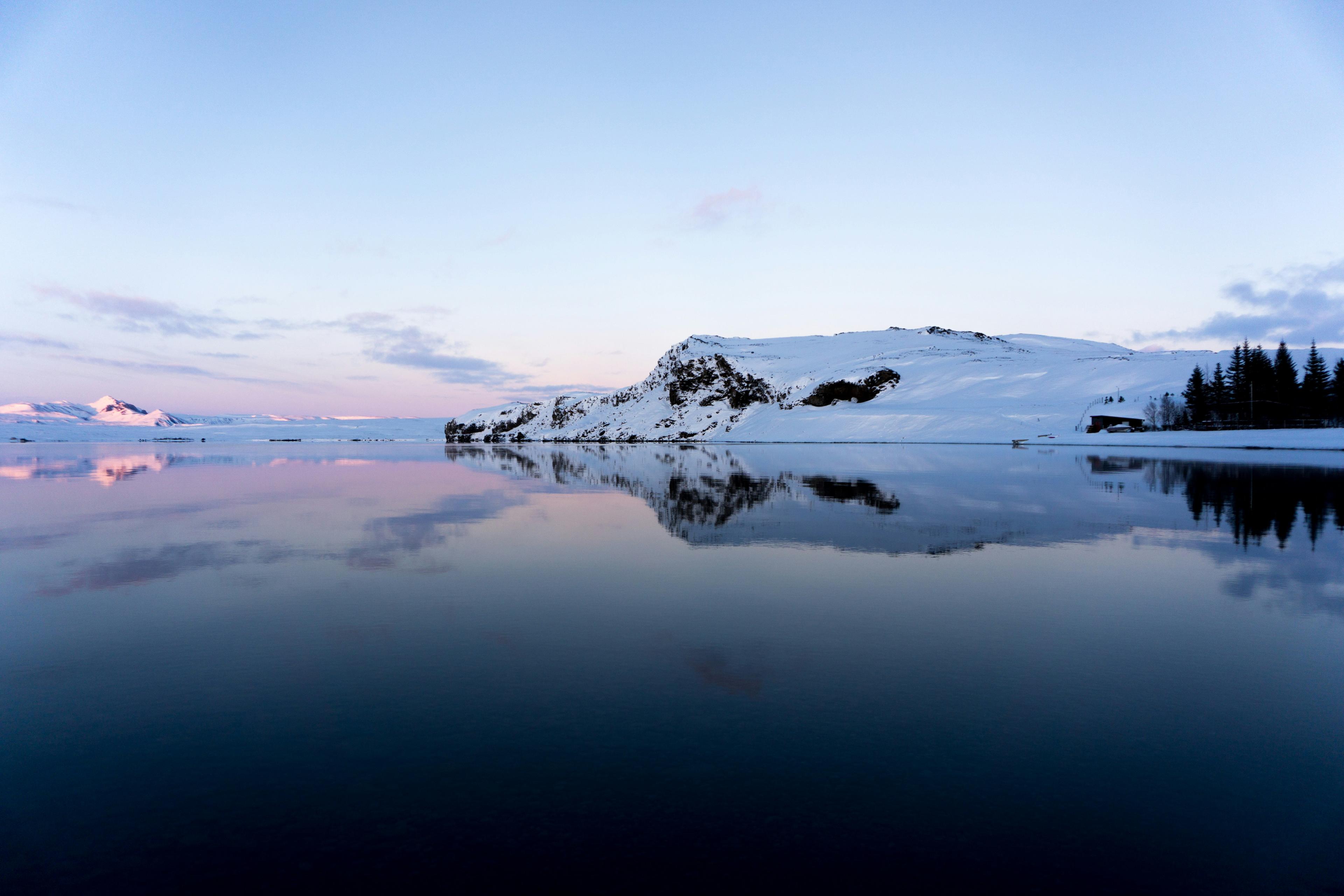 Serene lake reflecting a snow-covered mountain under a pastel-colored sky during sunset at Thingvallavatn.