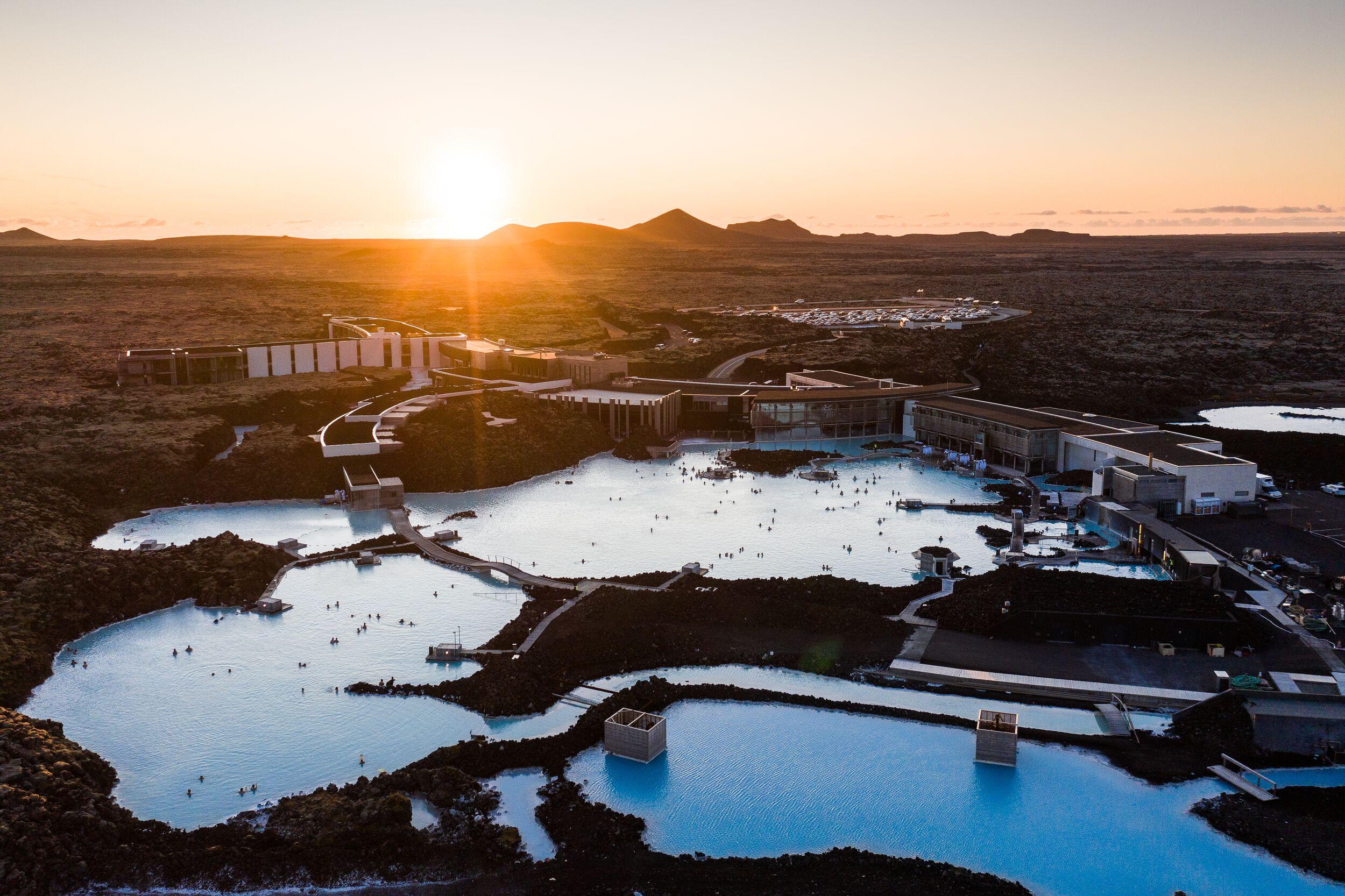 A scenic view of a geothermal spa surrounded by volcanic landscapes at sunset.