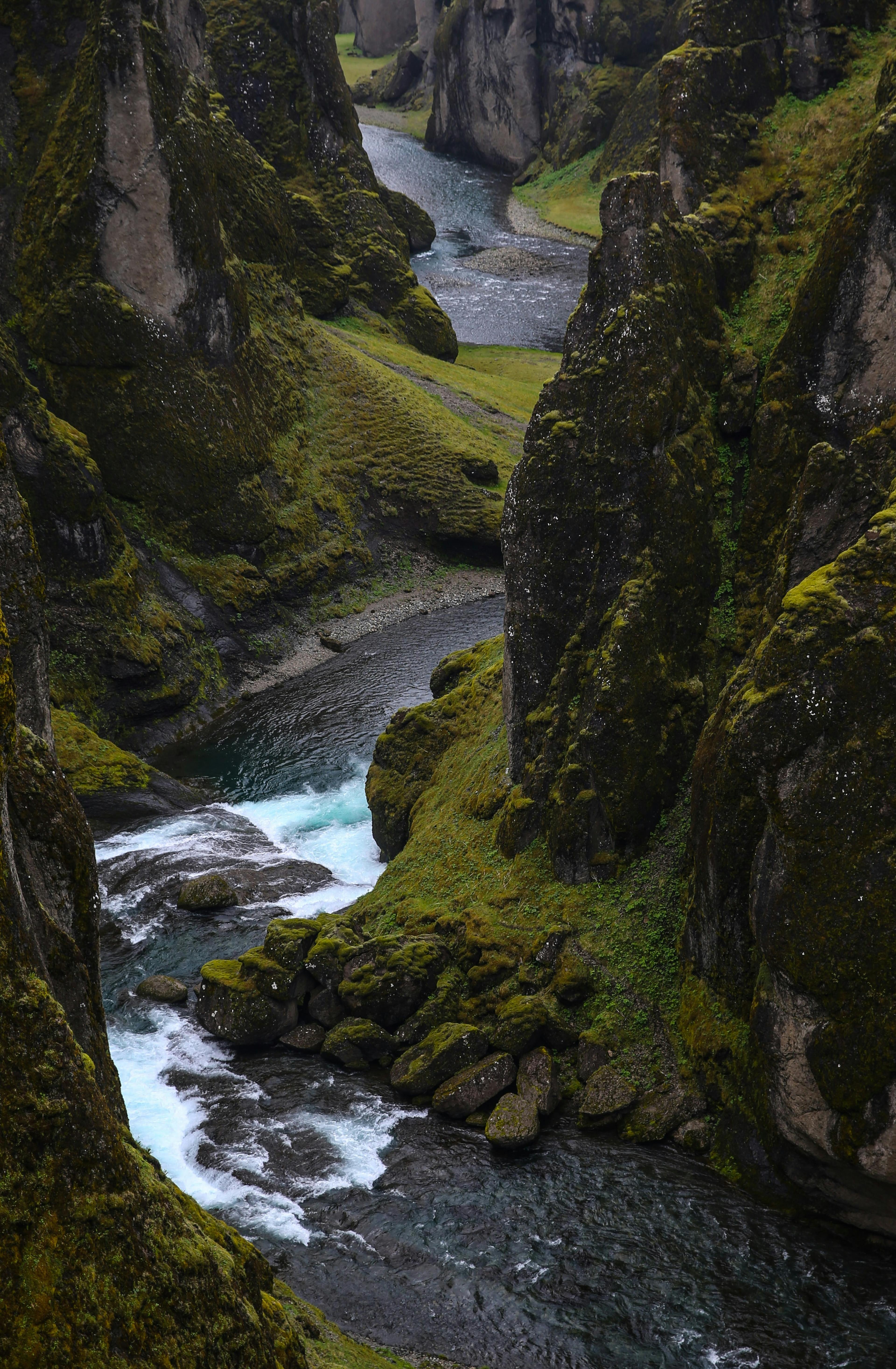 A rugged canyon with a winding river below, casting shadows and highlights on the mossy cliffs.
