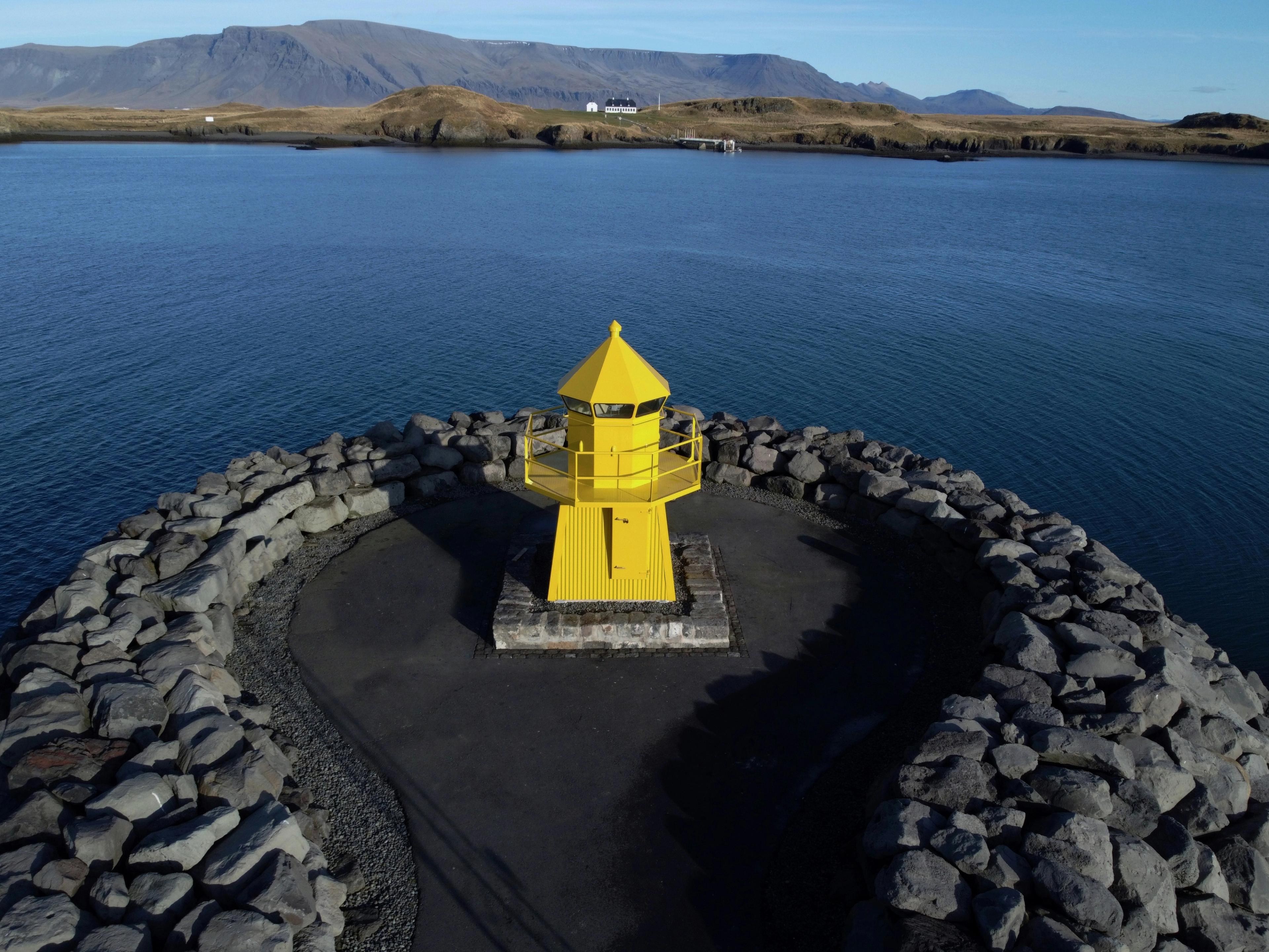 an aerial view of a yellow lighthouse in the middle of a body of water .