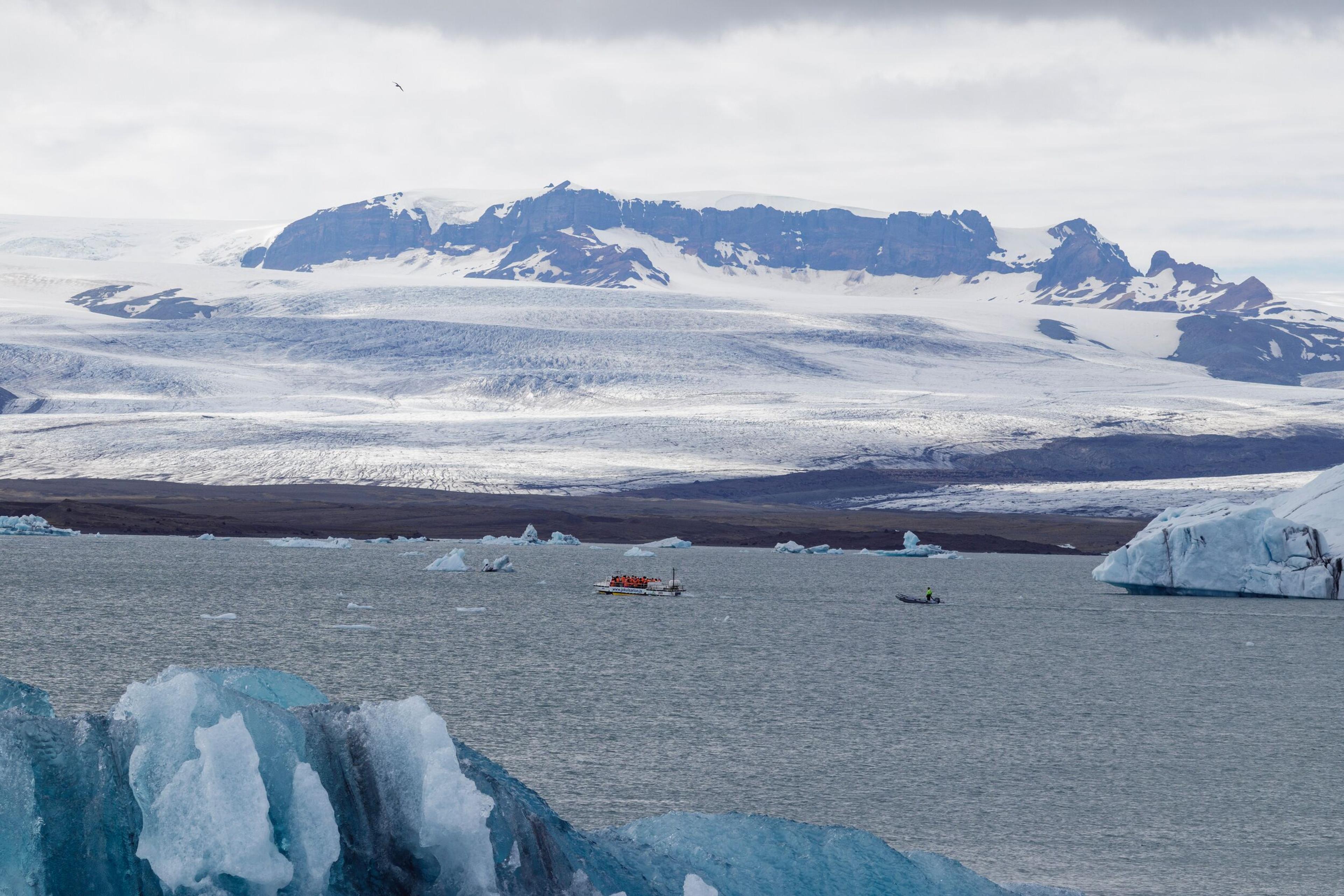 Glacial lagoon with icebergs, two boats, and a glacier in the background.