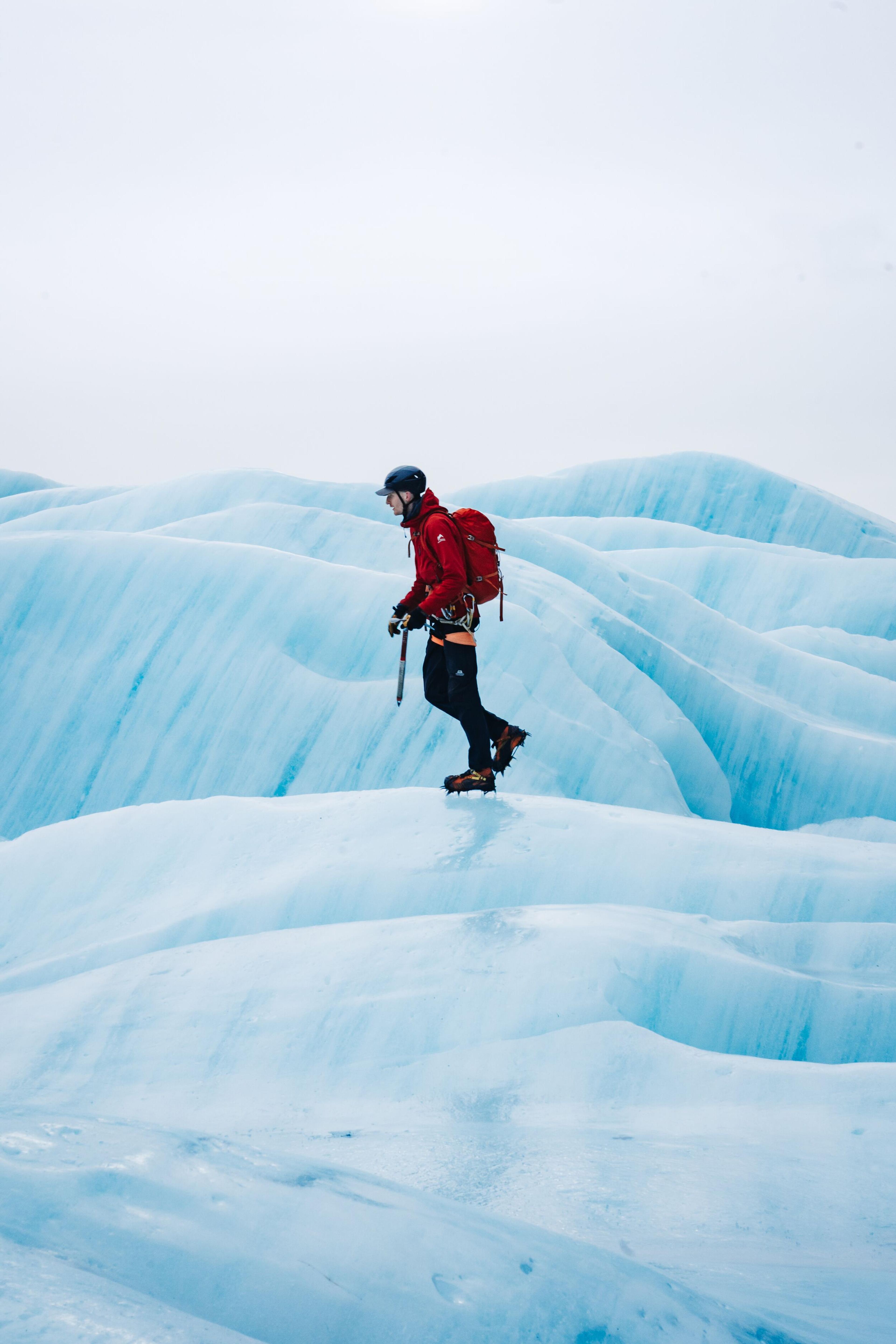Man in red jacket ice climbing on a blue glacier in Iceland.