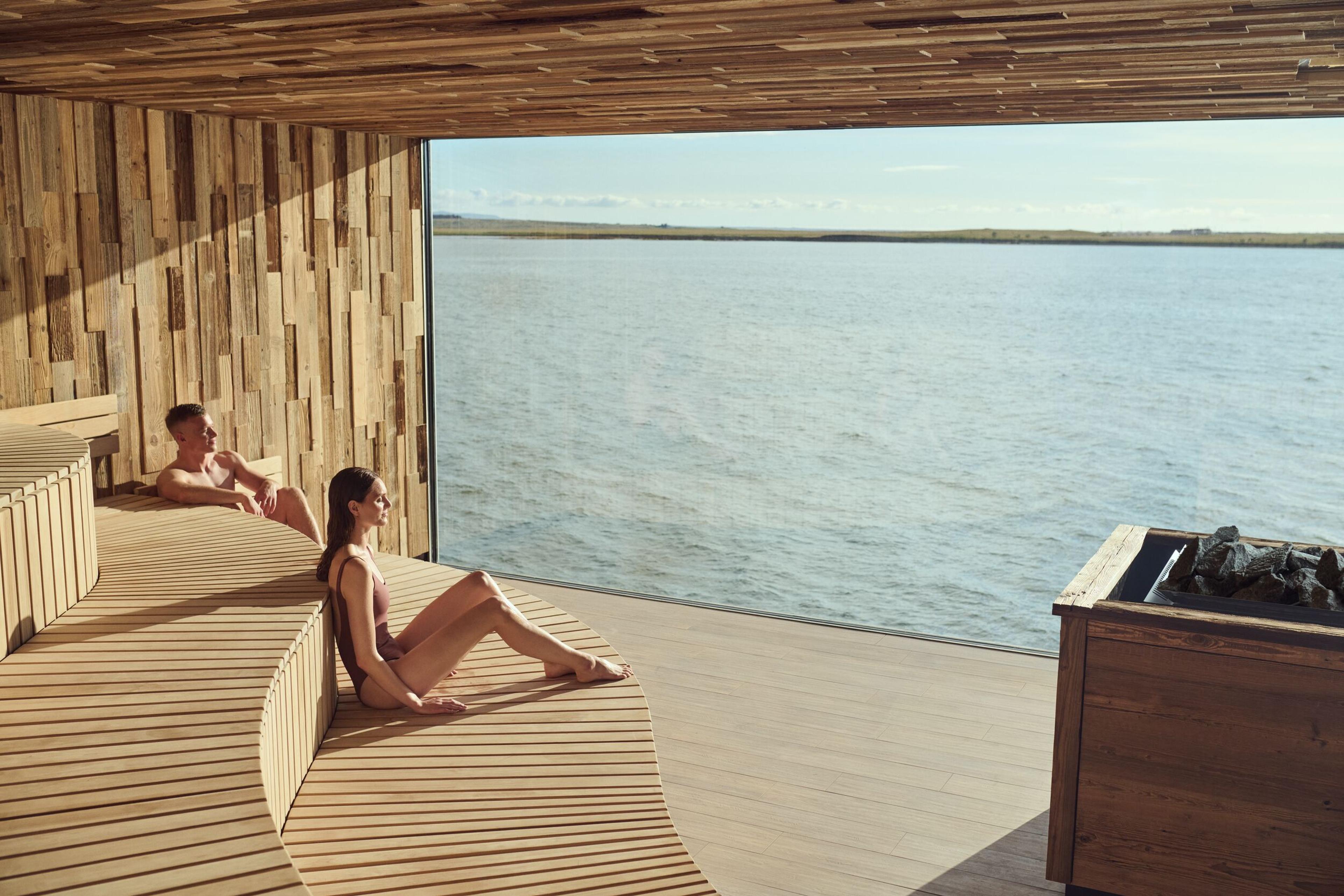 a man and a woman are sitting in a sauna overlooking the ocean .