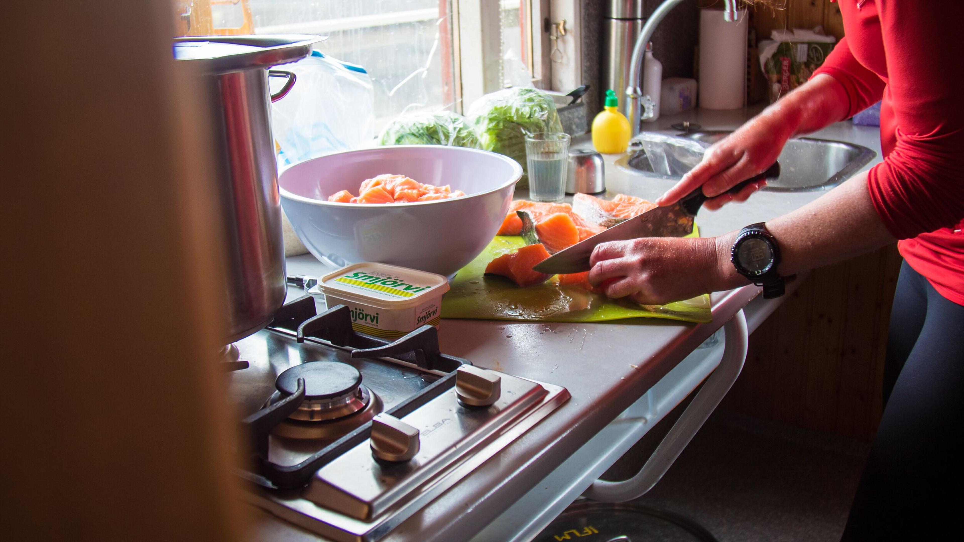 A person slicing salmon on a cutting board in a kitchen.